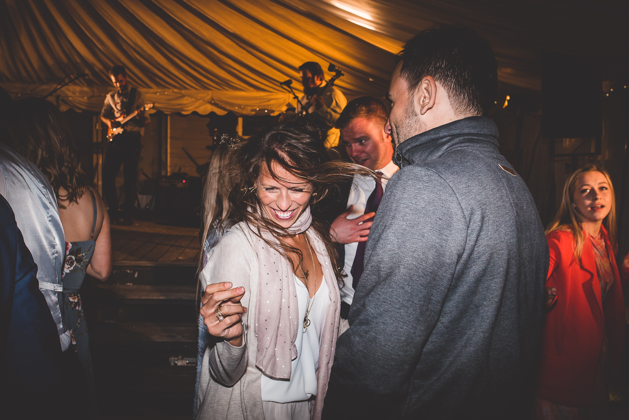 A group of people, including the bride, dancing at a wedding party in a tent.