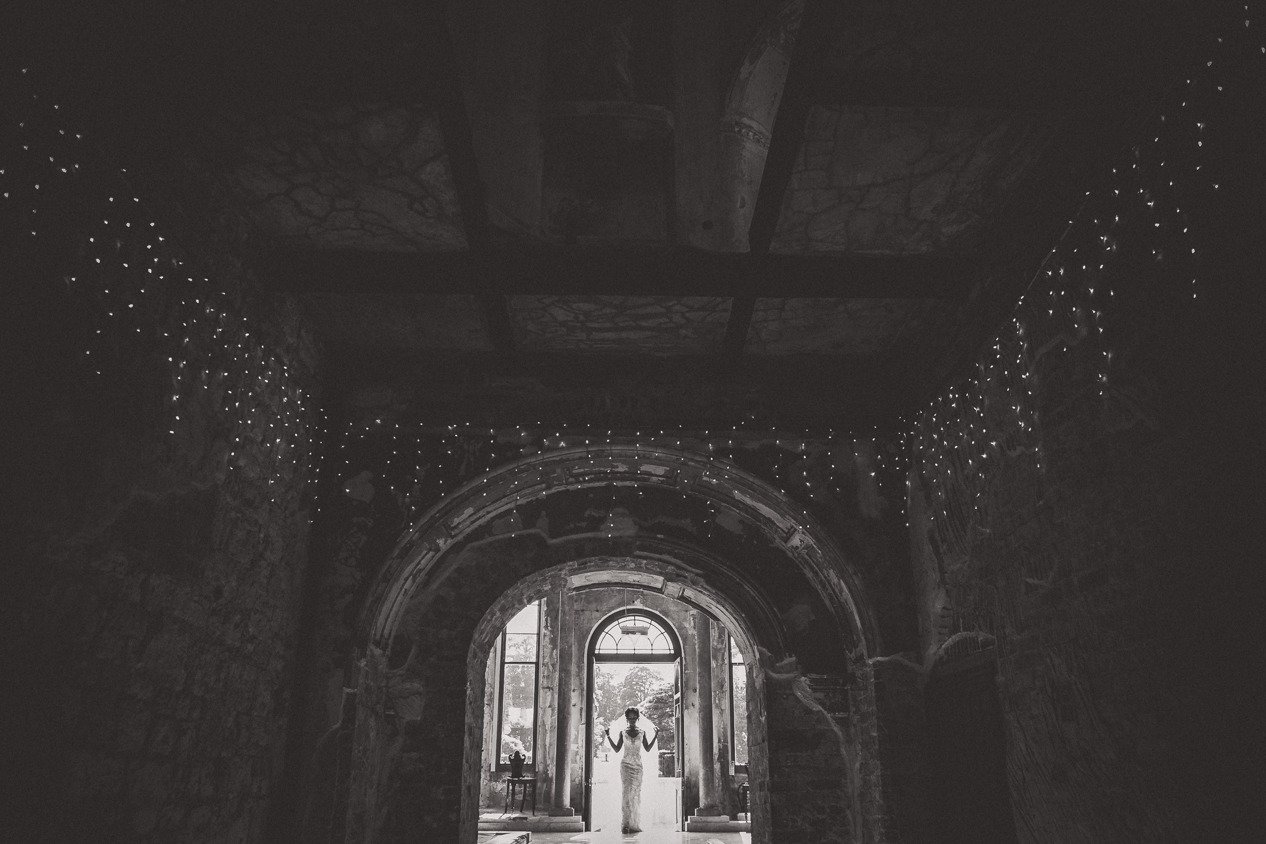 A black and white wedding photo of a bride and groom standing in an archway.