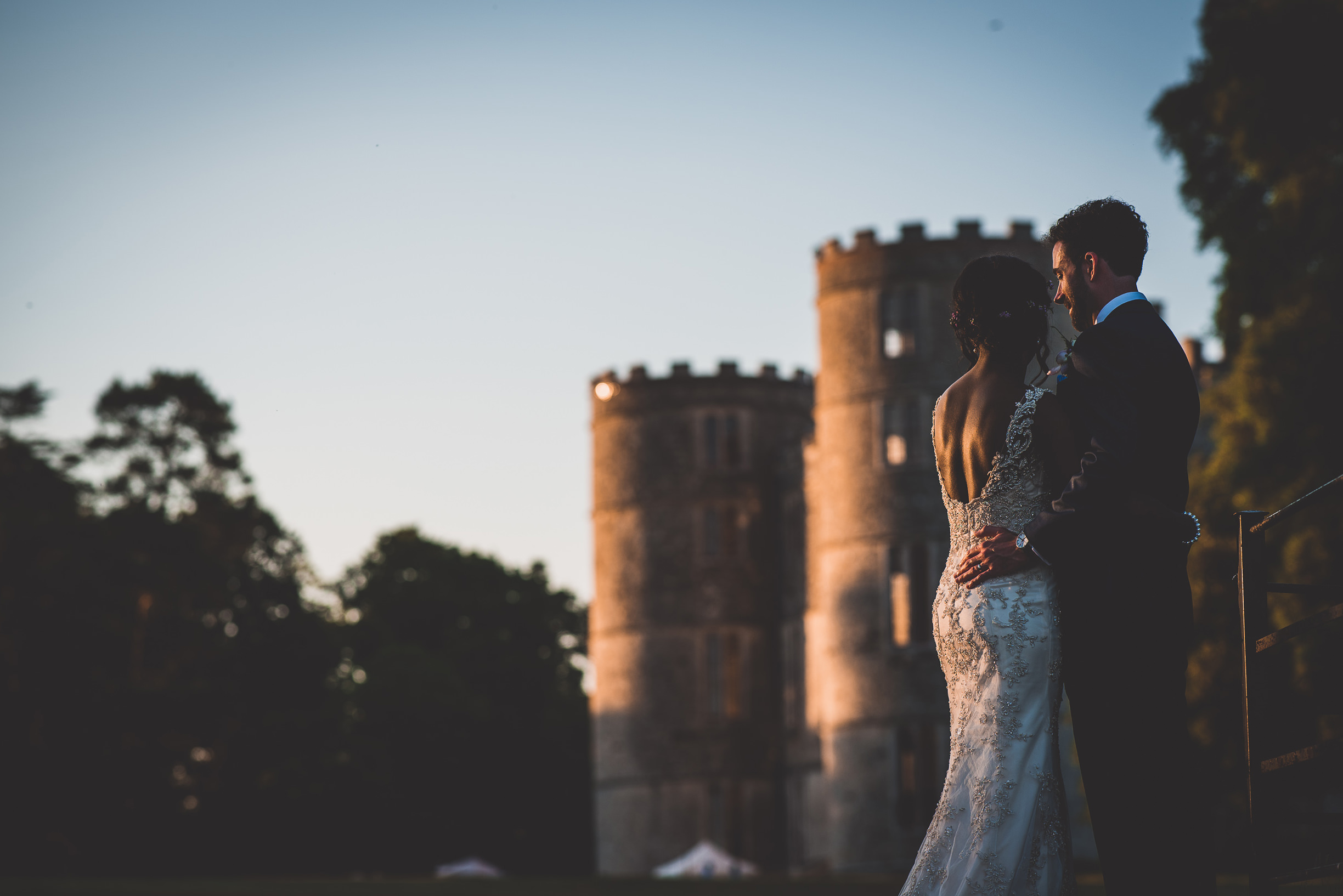 A wedding couple posing for their photographer in front of a castle.