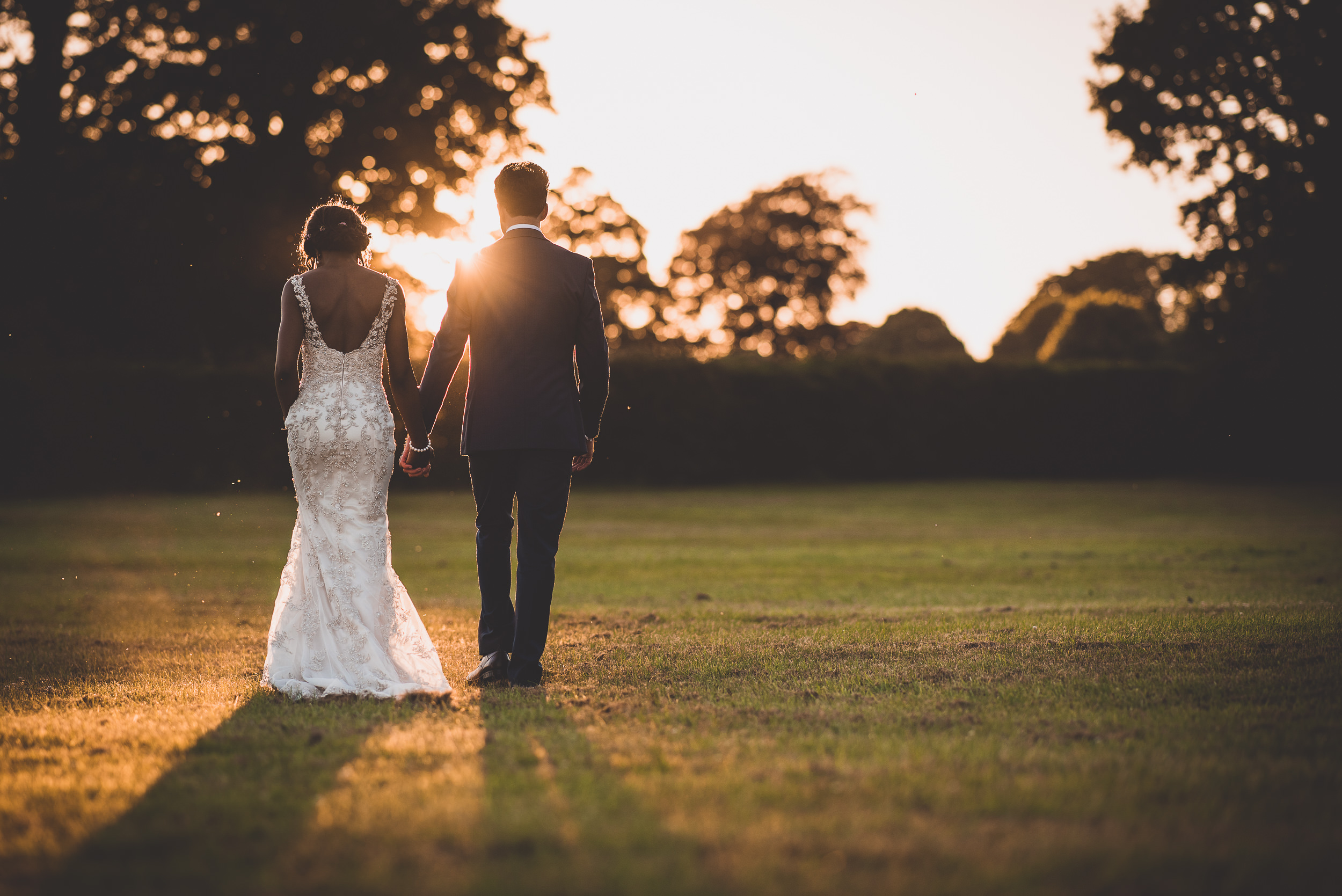 A wedding couple elegantly strolling in a scenic field during sunset.