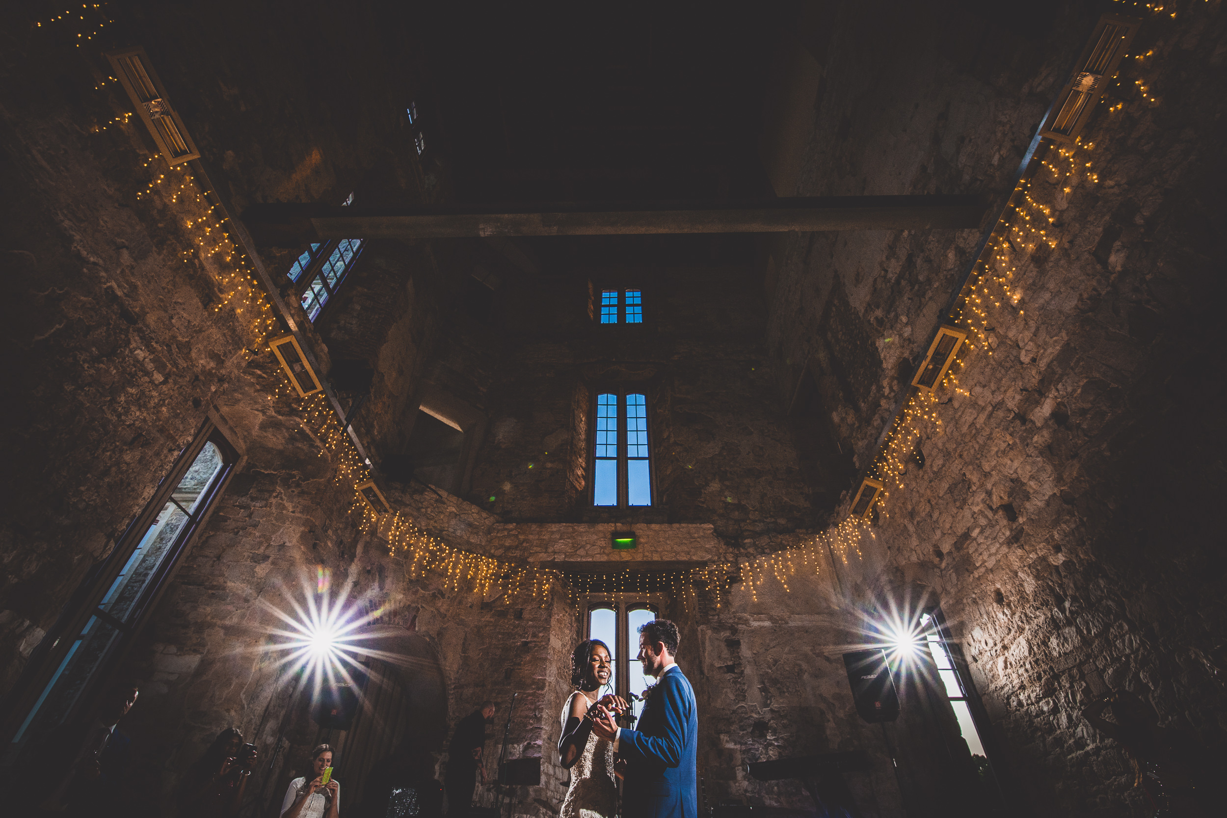 A groom standing with his bride in a dimly lit wedding room.