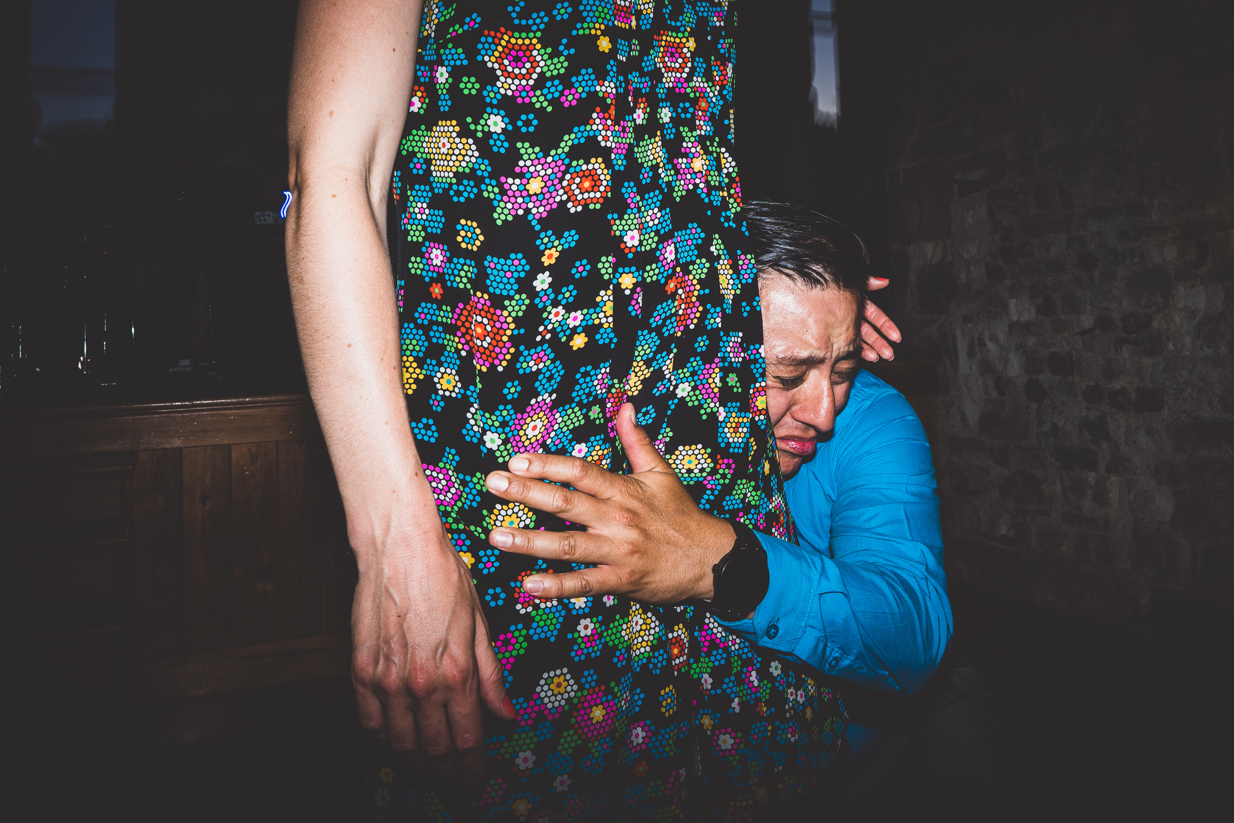 A wedding photographer captures a bride hugging a man in a floral dress.