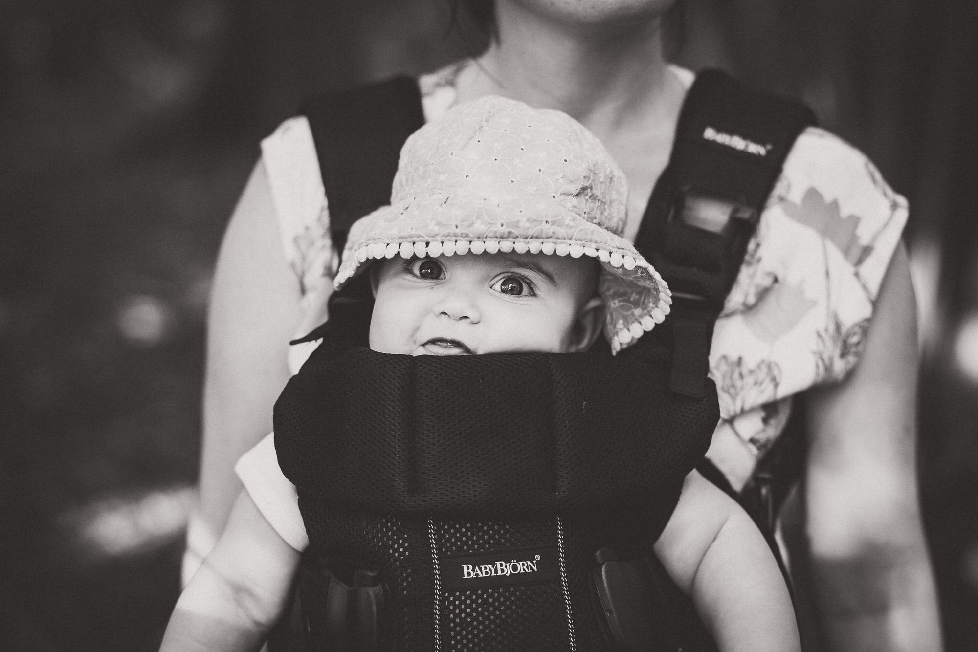A wedding photographer captures a beautiful moment of a woman holding a baby in a baby carrier during the groom's wedding photo session.