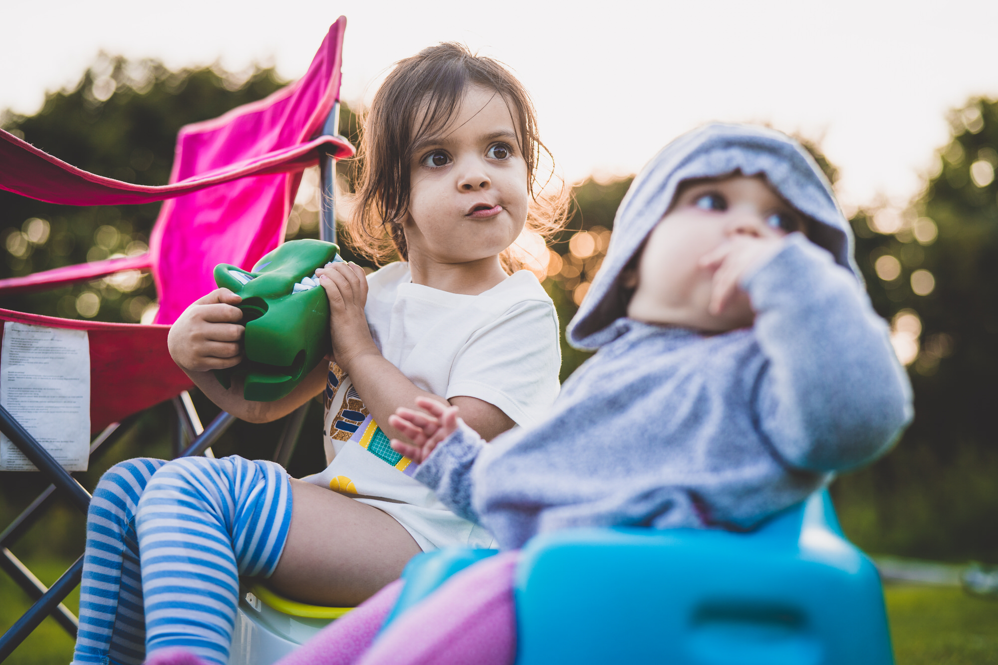 Two little girls dressed as a bride and groom sitting on a potty in a grassy area.