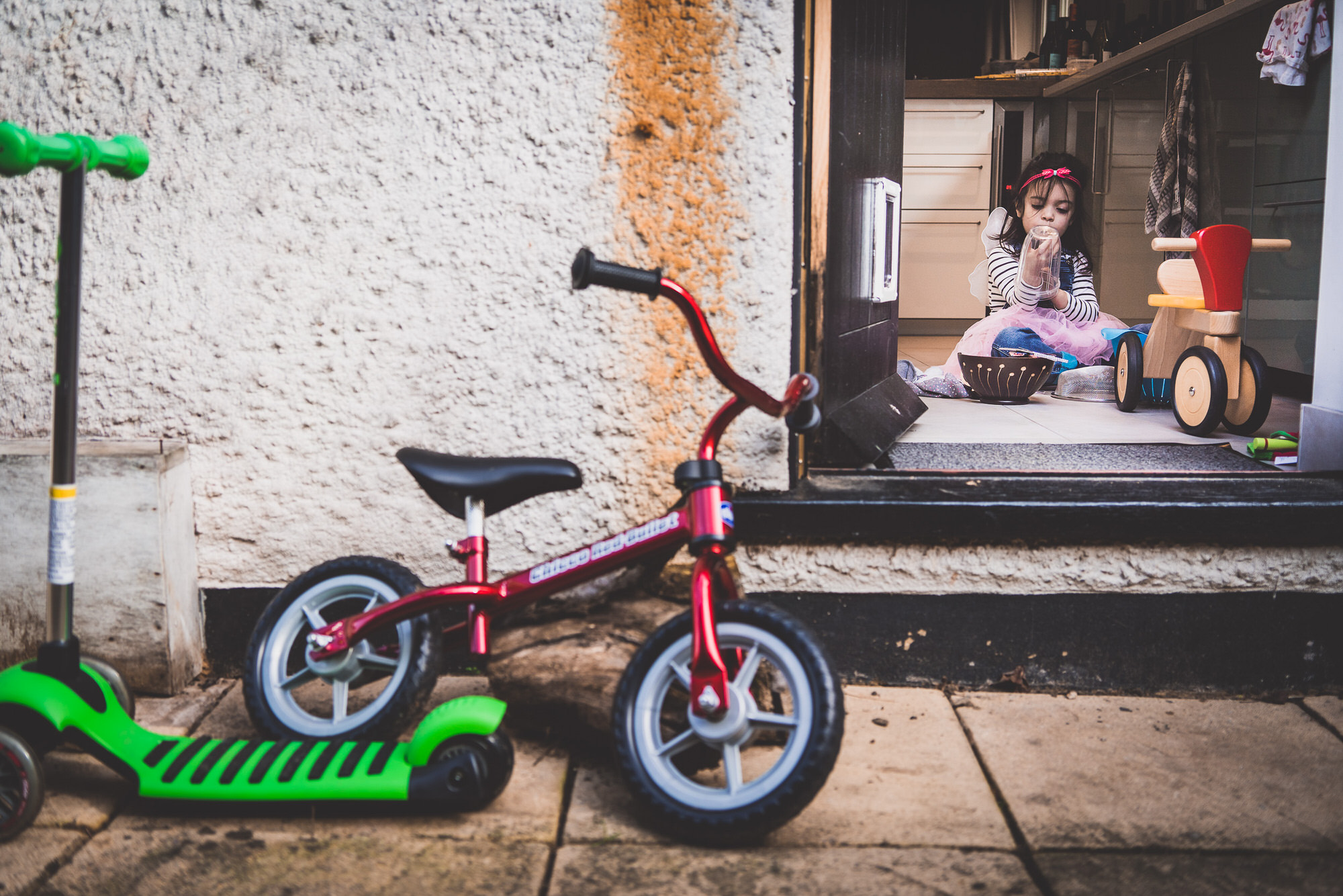 A little girl on a scooter passing by a house while a wedding photographer captivates the moment.