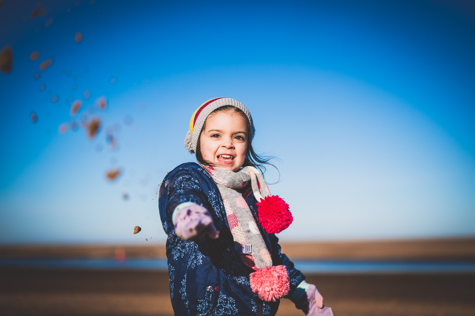 A little girl tossing sand during a wedding on the beach for a unique wedding photo.