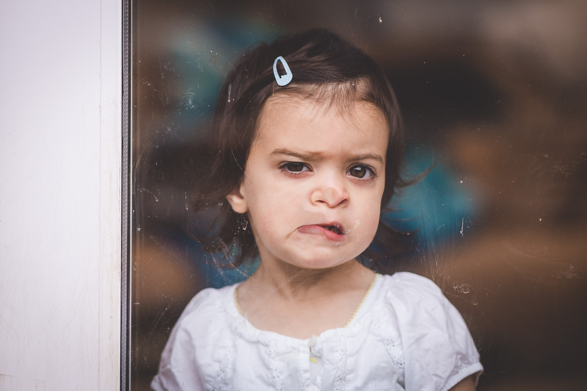 A little girl, dressed as a flower girl, looking out of a window at a wedding.