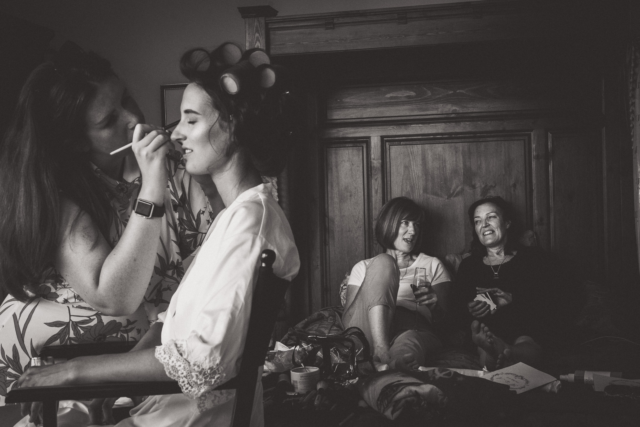 A wedding photographer captures a black and white photo of a bride getting ready in a room.