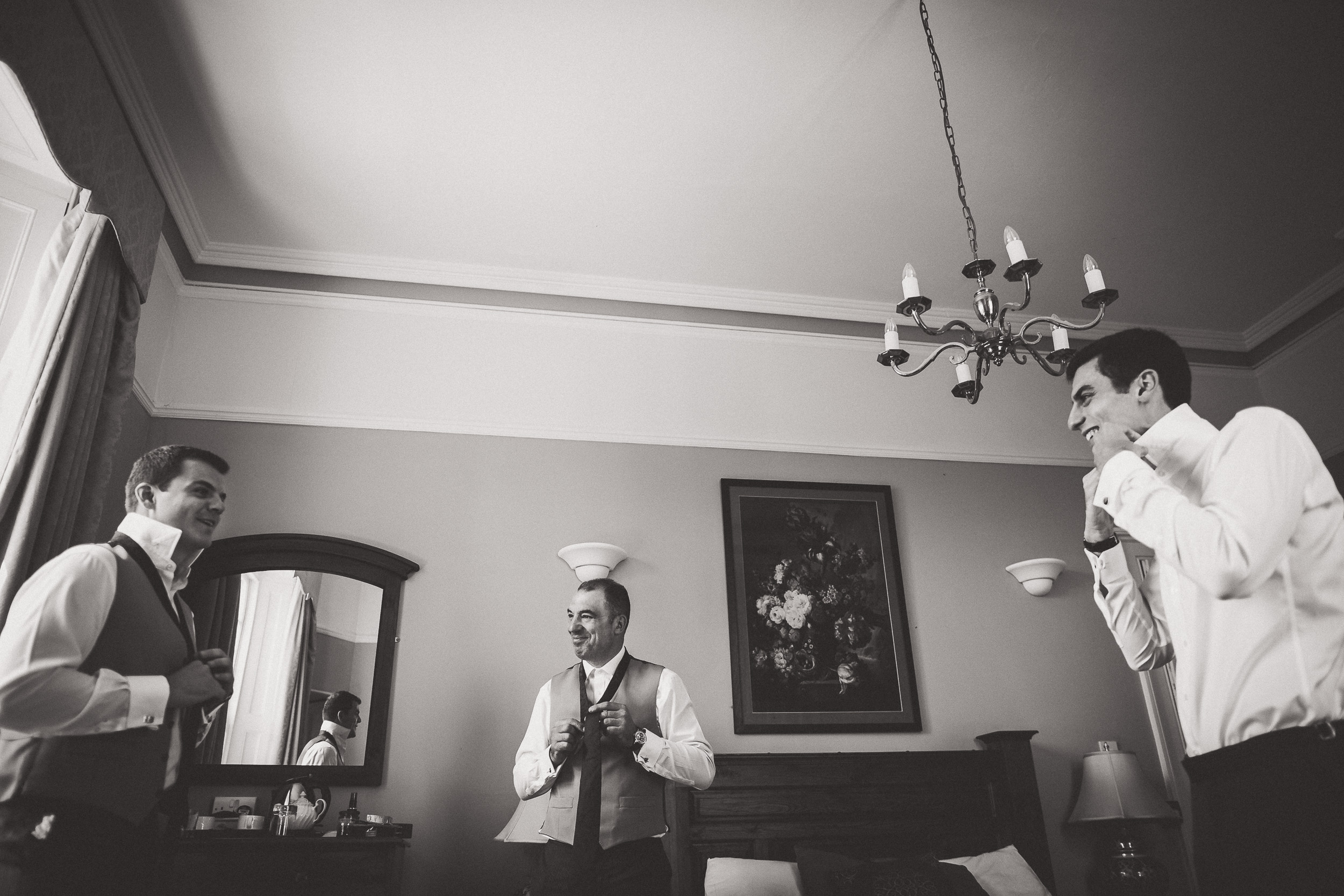 A black and white photo of men getting ready for a wedding in a room.