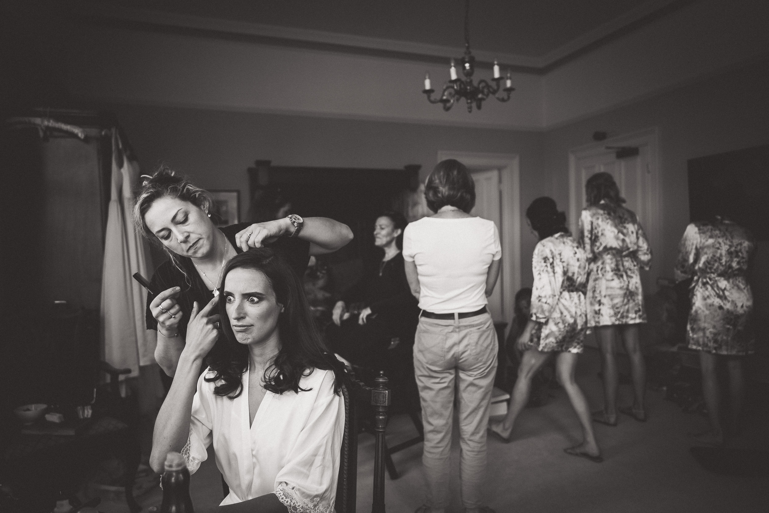 A bride prepares for her wedding day, getting her hair done in a room filled with excitement and anticipation.