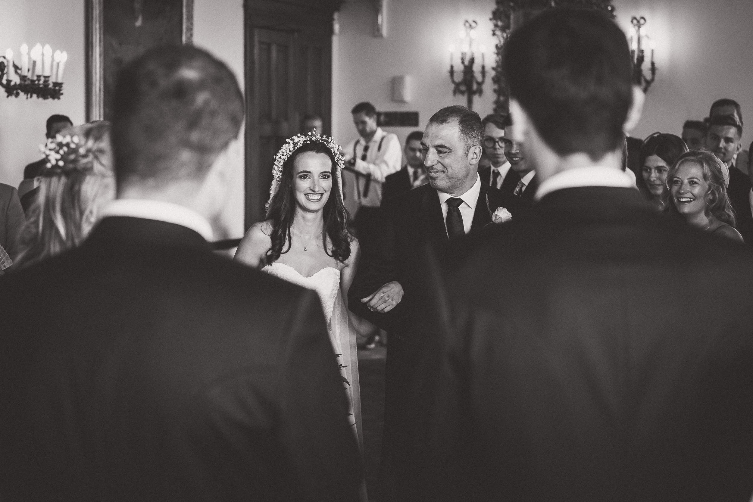 A wedding photographer captures a black and white photo of a bride and groom walking down the aisle.