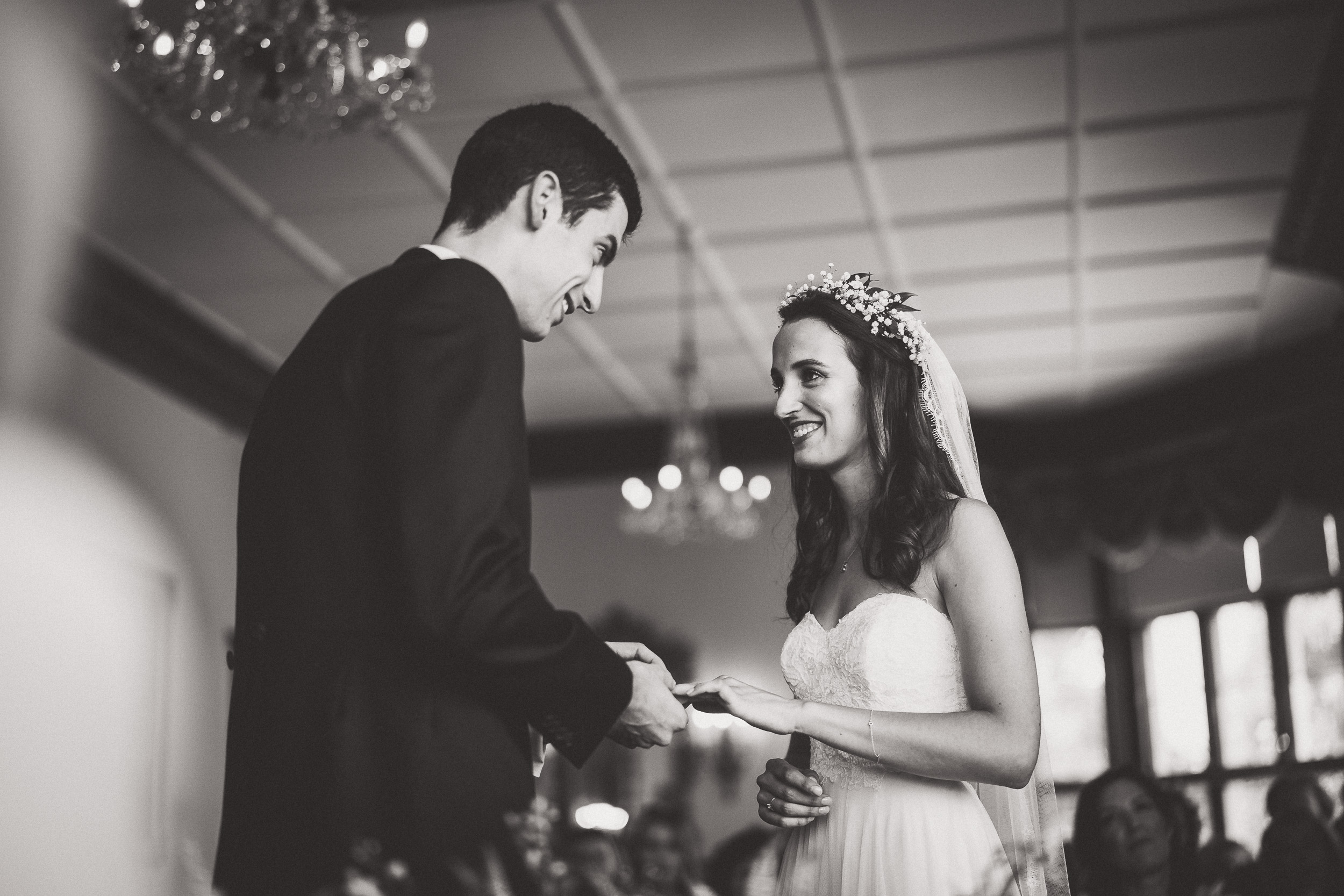 A wedding photographer captures a bride and groom exchanging rings in a black and white photo.