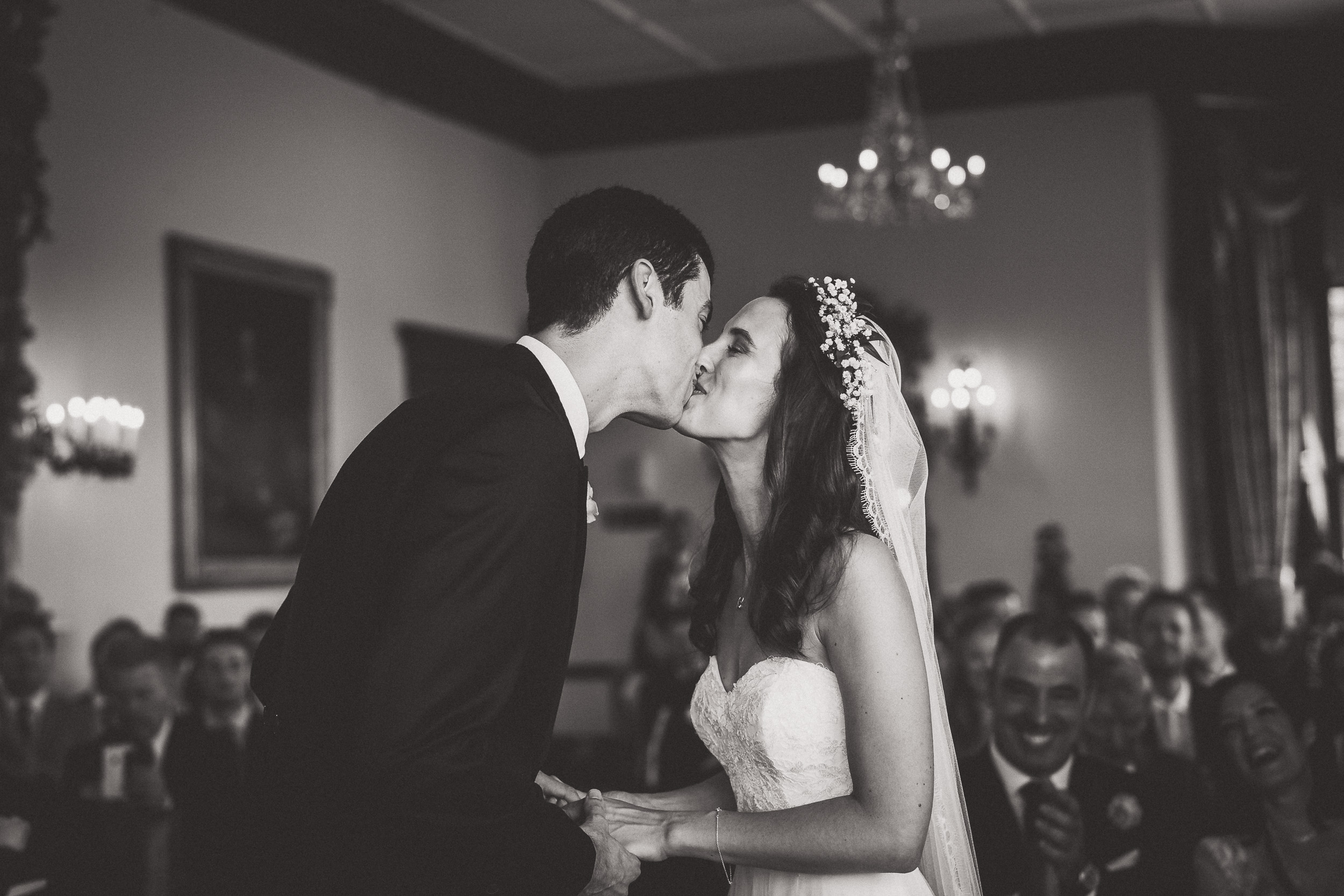 A wedding photographer captures a sweet moment as the groom and bride share a kiss during their ceremony.