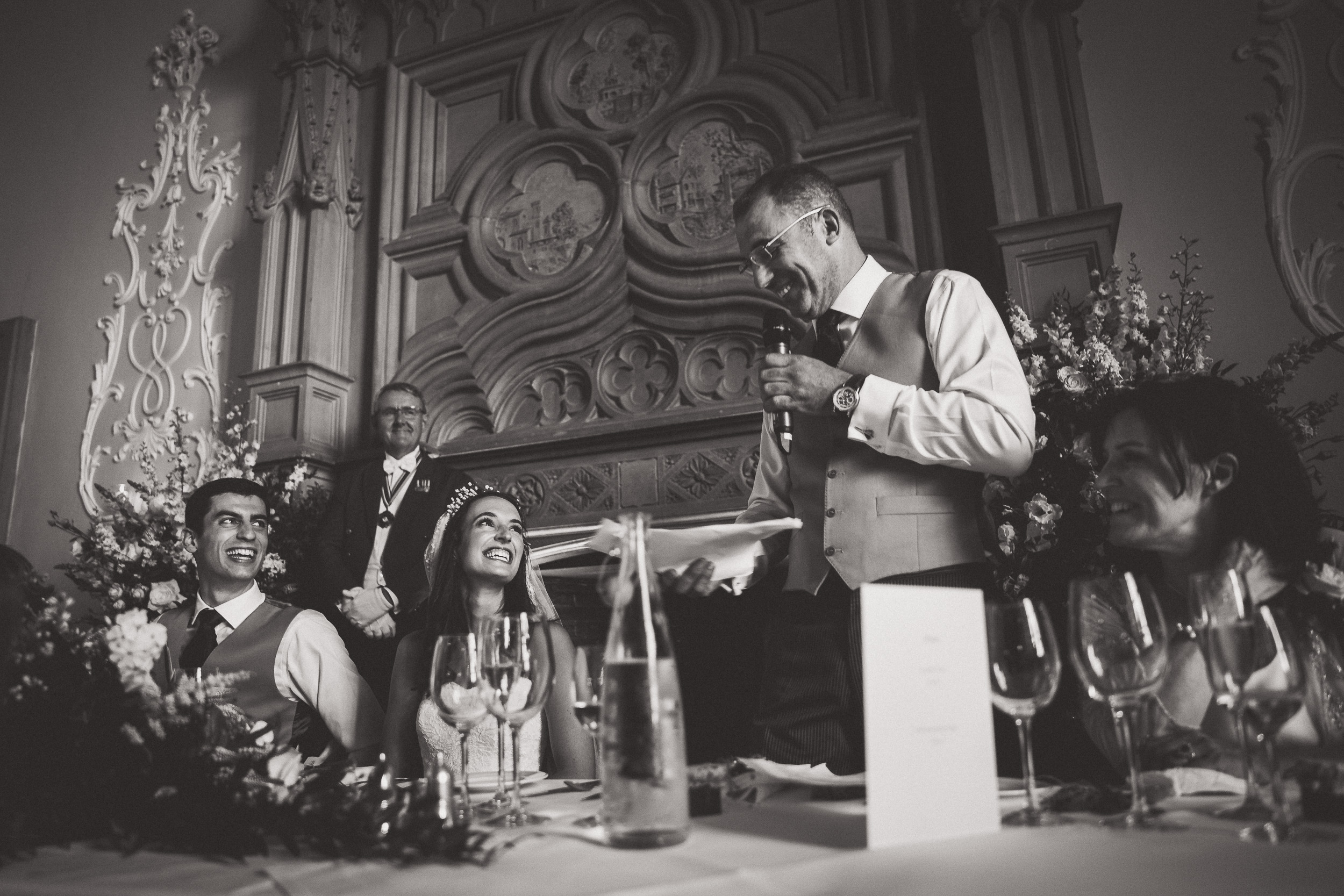 A wedding photographer captures a black and white wedding photo of a man giving a speech.