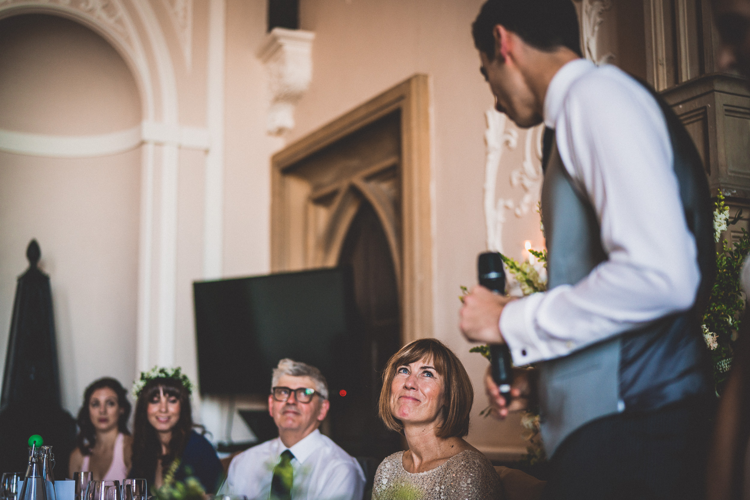 A wedding photographer captures moments as a man delivers a heartfelt speech at the bride's ceremony.