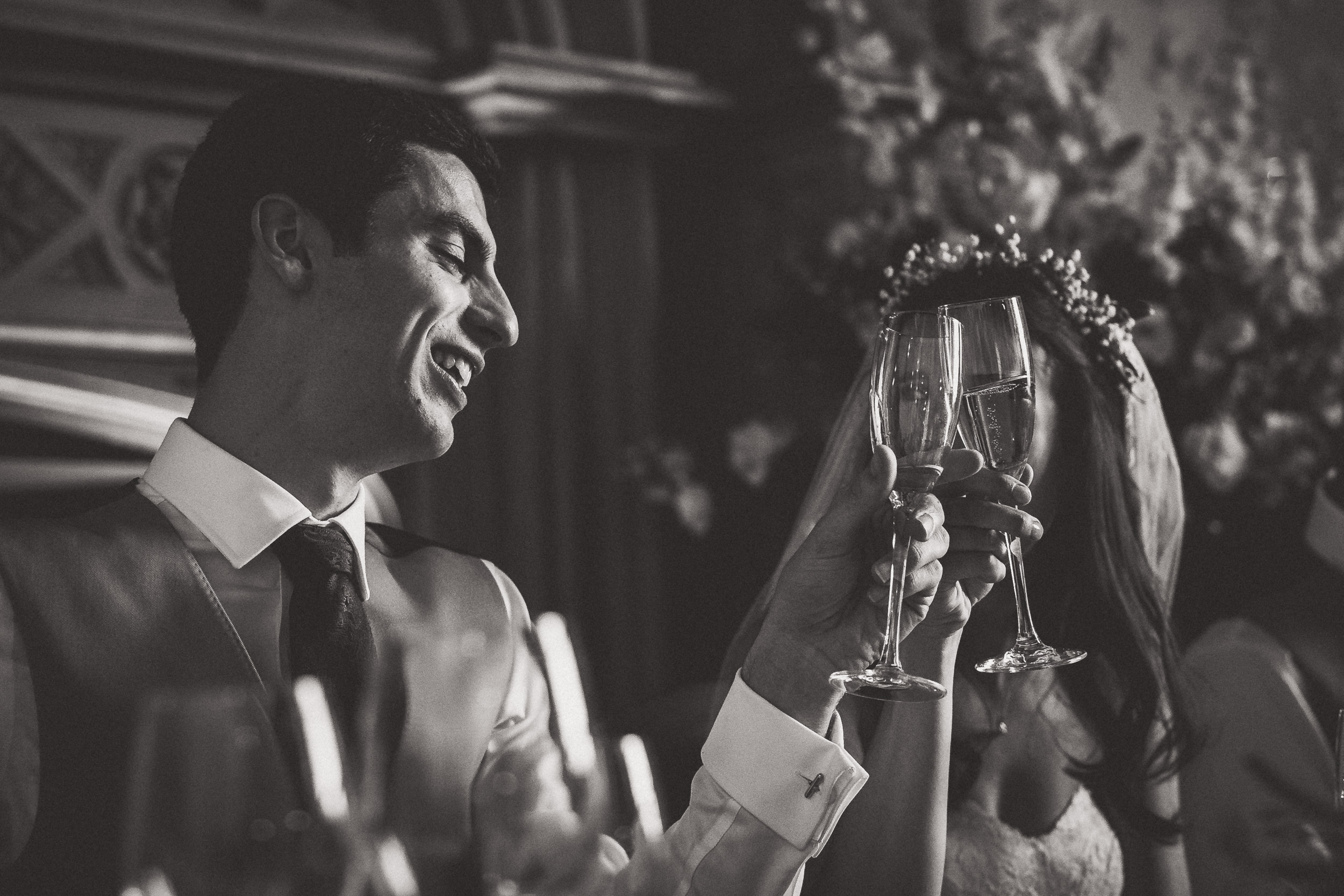 Black and white wedding photo of bride and groom toasting glasses.