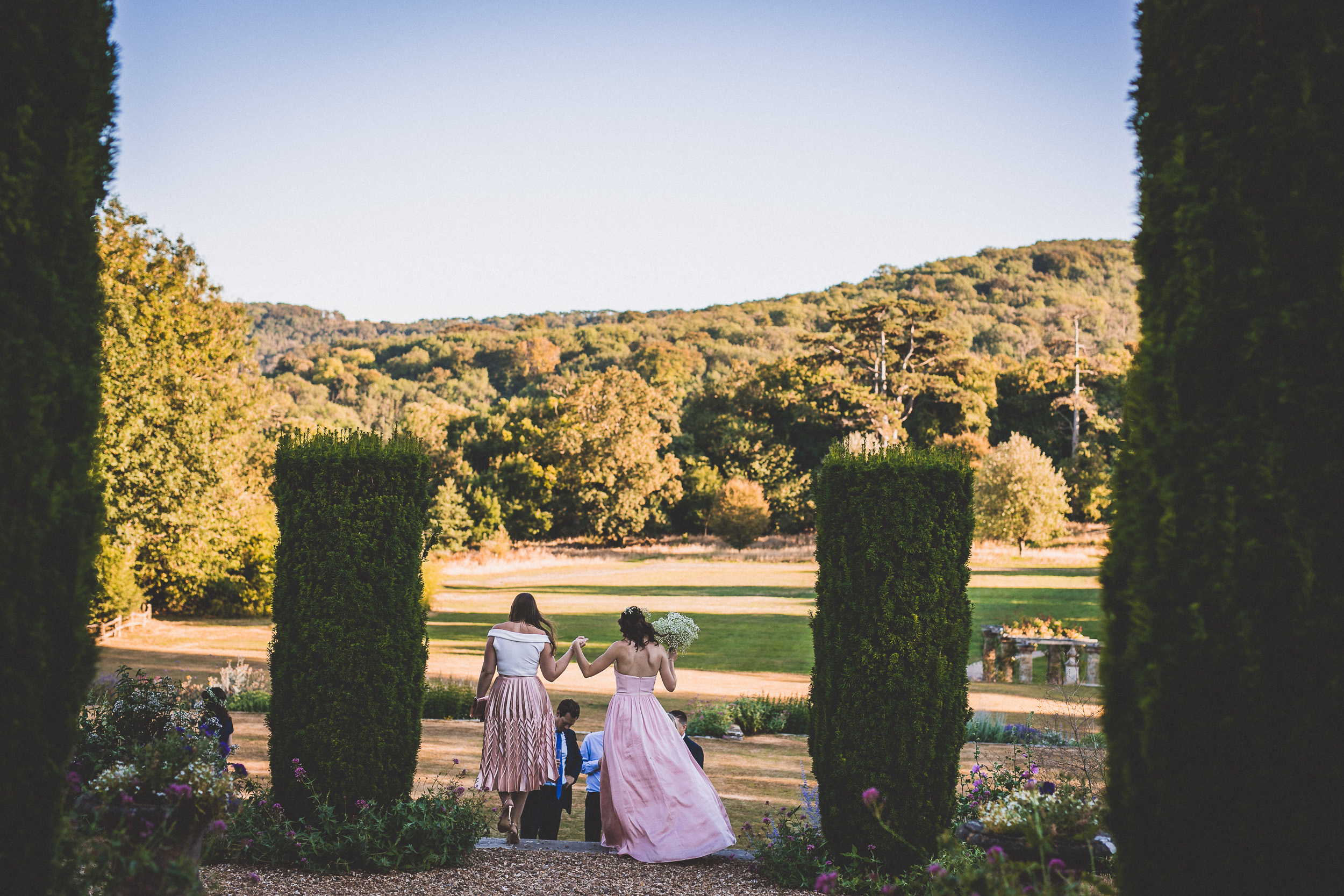 A wedding photographer captures a bride and her bridesmaids walking through a garden for a wedding photo.