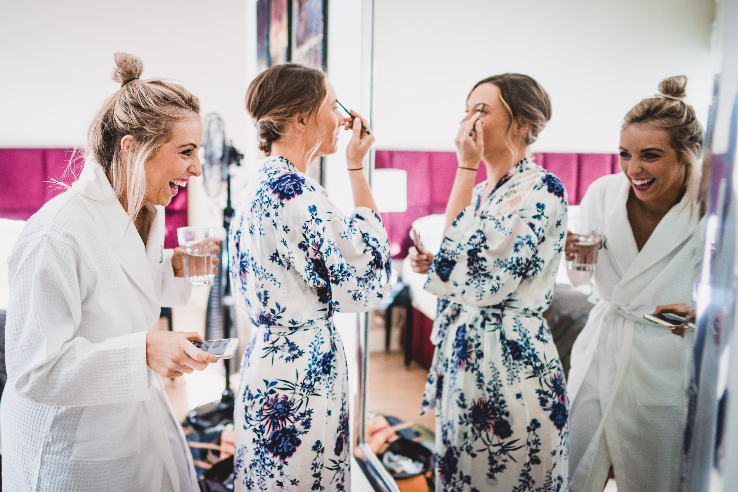 Three bridesmaids getting ready for the wedding and admiring their robes in front of a mirror.