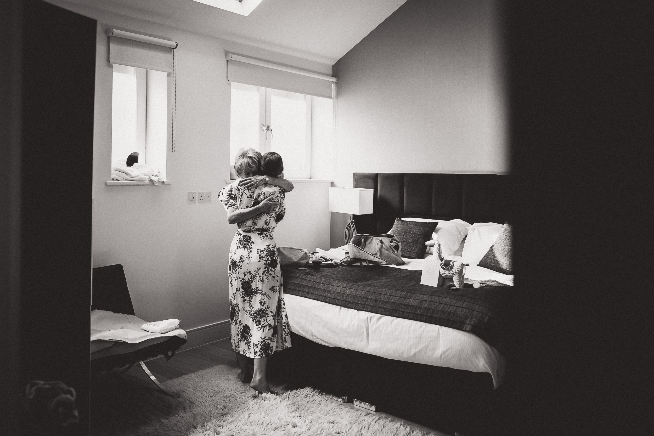 A wedding photographer captures a woman in front of a bed in a black and white wedding photo.