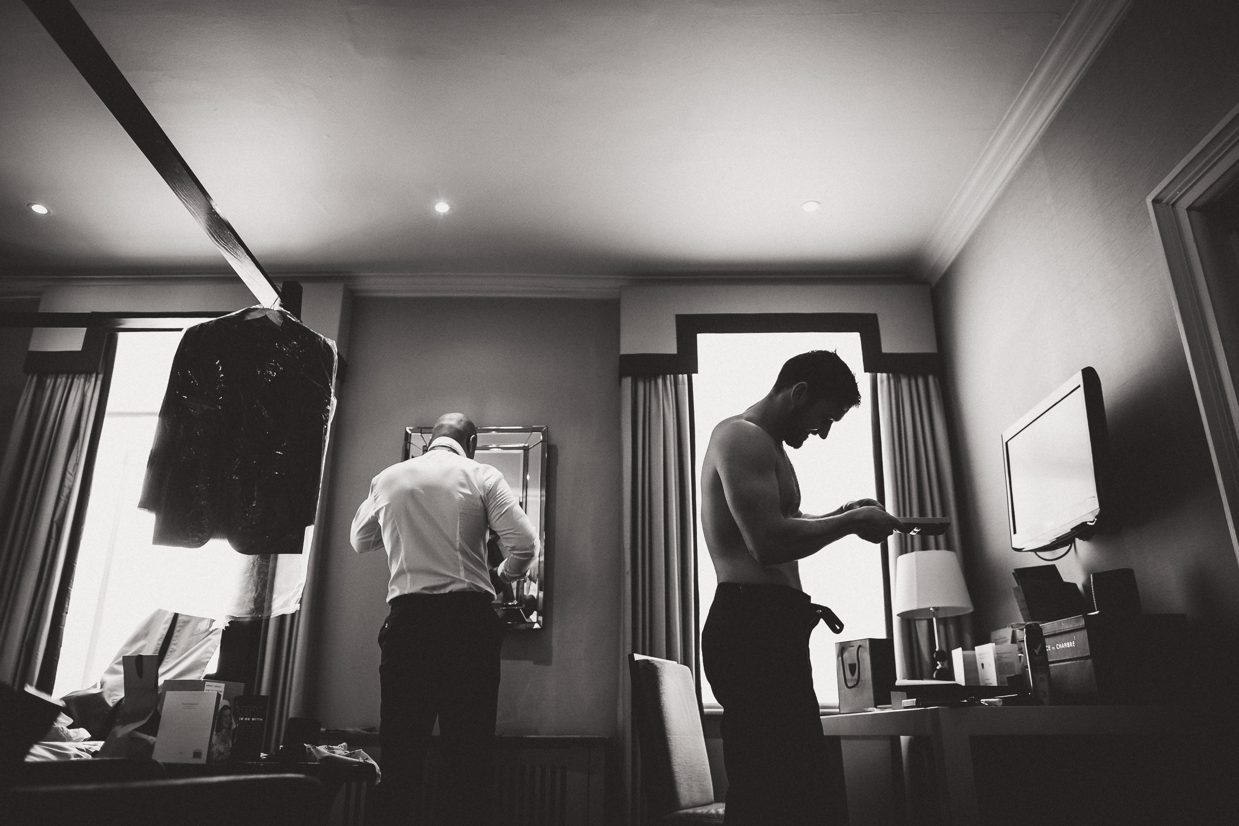 A black and white photo of a groom getting ready in a hotel room.