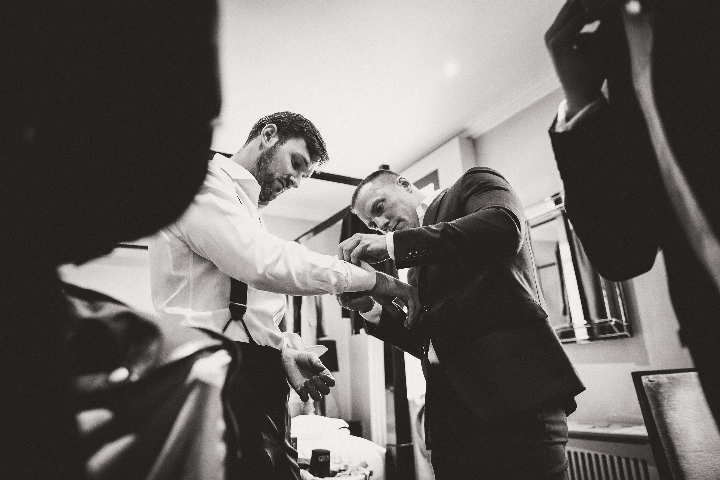 A groom is adjusting his tie in a wedding photo.