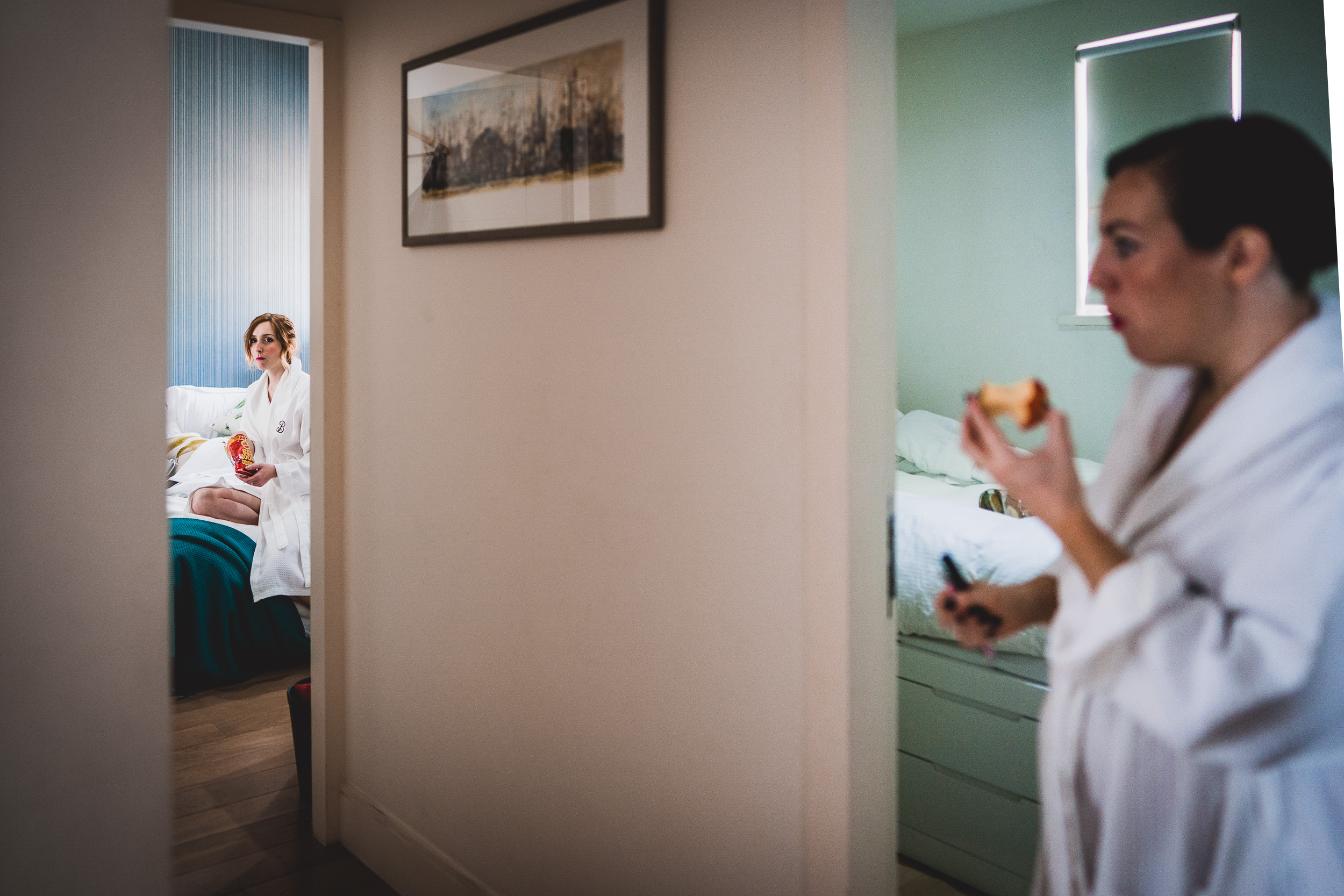 A bride in a white robe is eating a piece of bread in front of a mirror.