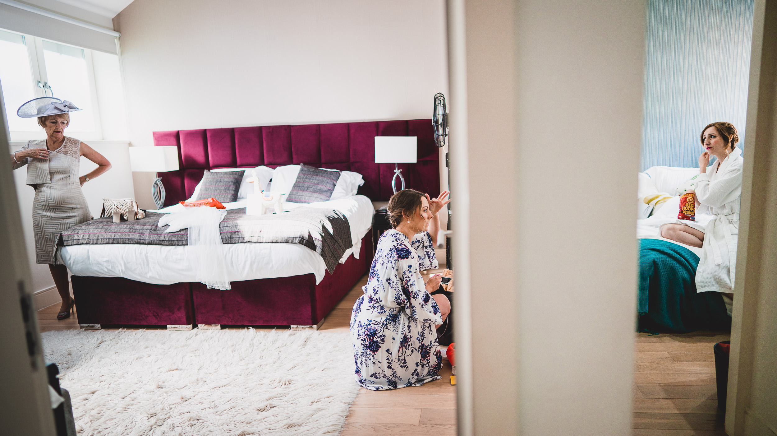 Bride and bridesmaids preparing for wedding photo in hotel room.