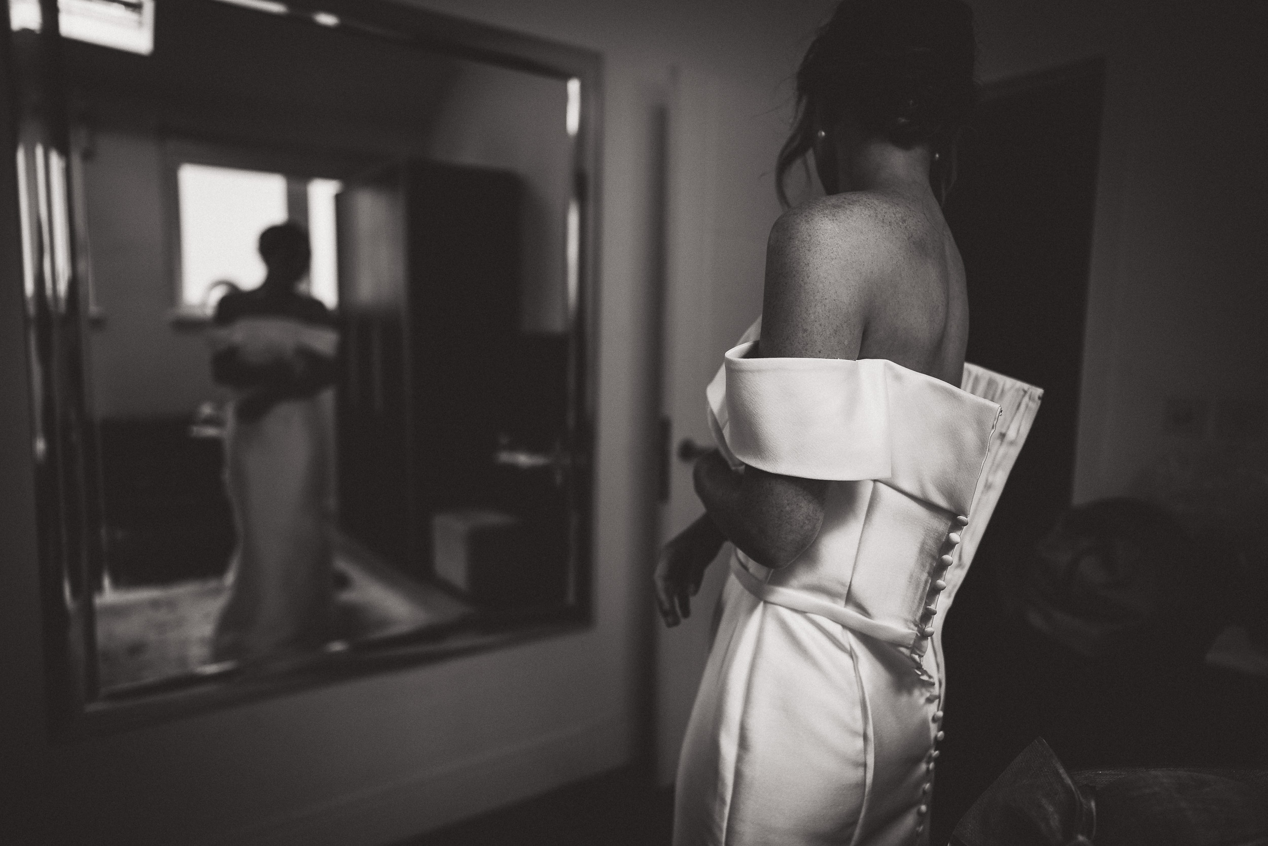 A bride, groom, and wedding photographer captured the intimate moment of the bride admiring herself in the mirror.