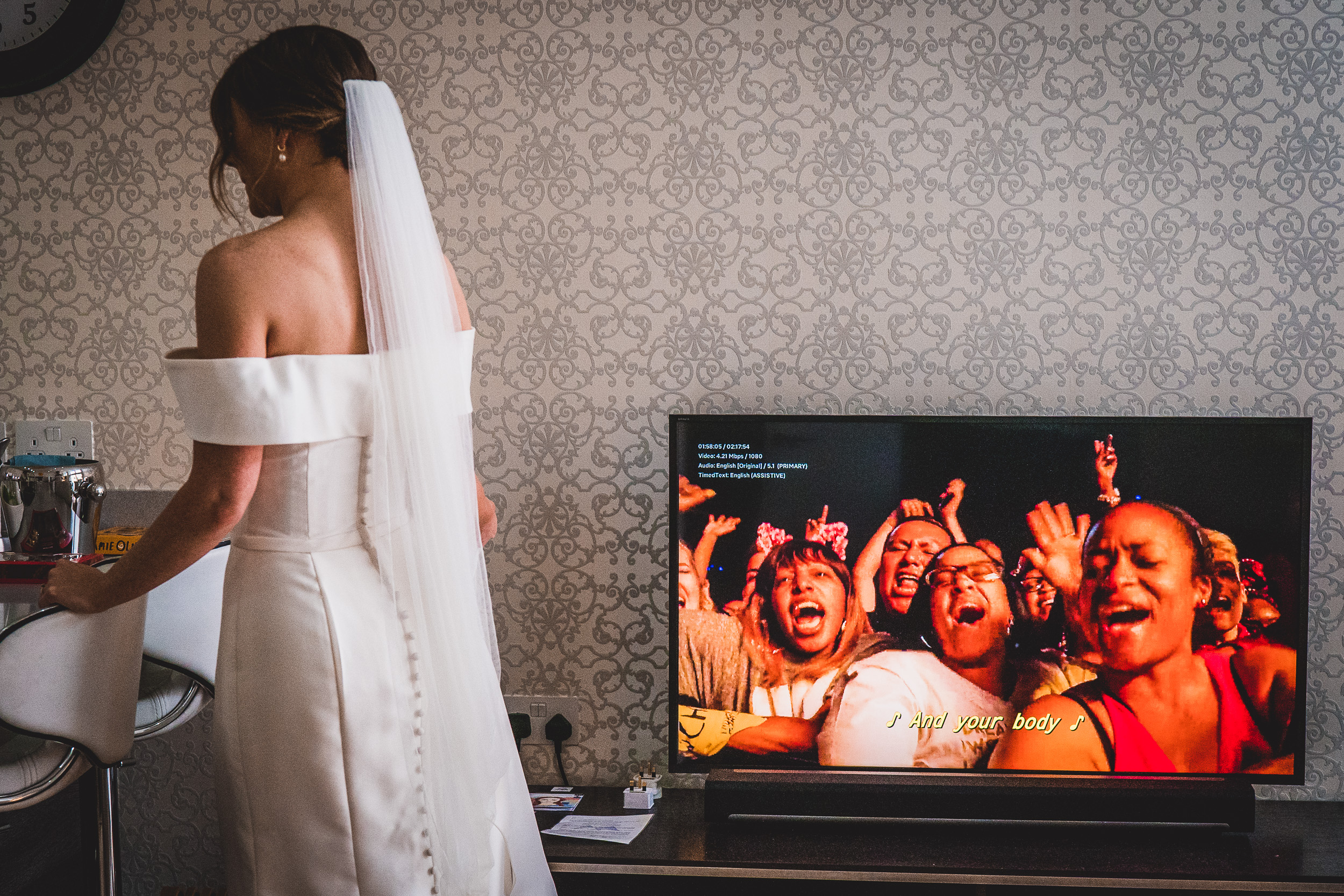 A bride in a wedding dress looking at a wedding photo on a TV.