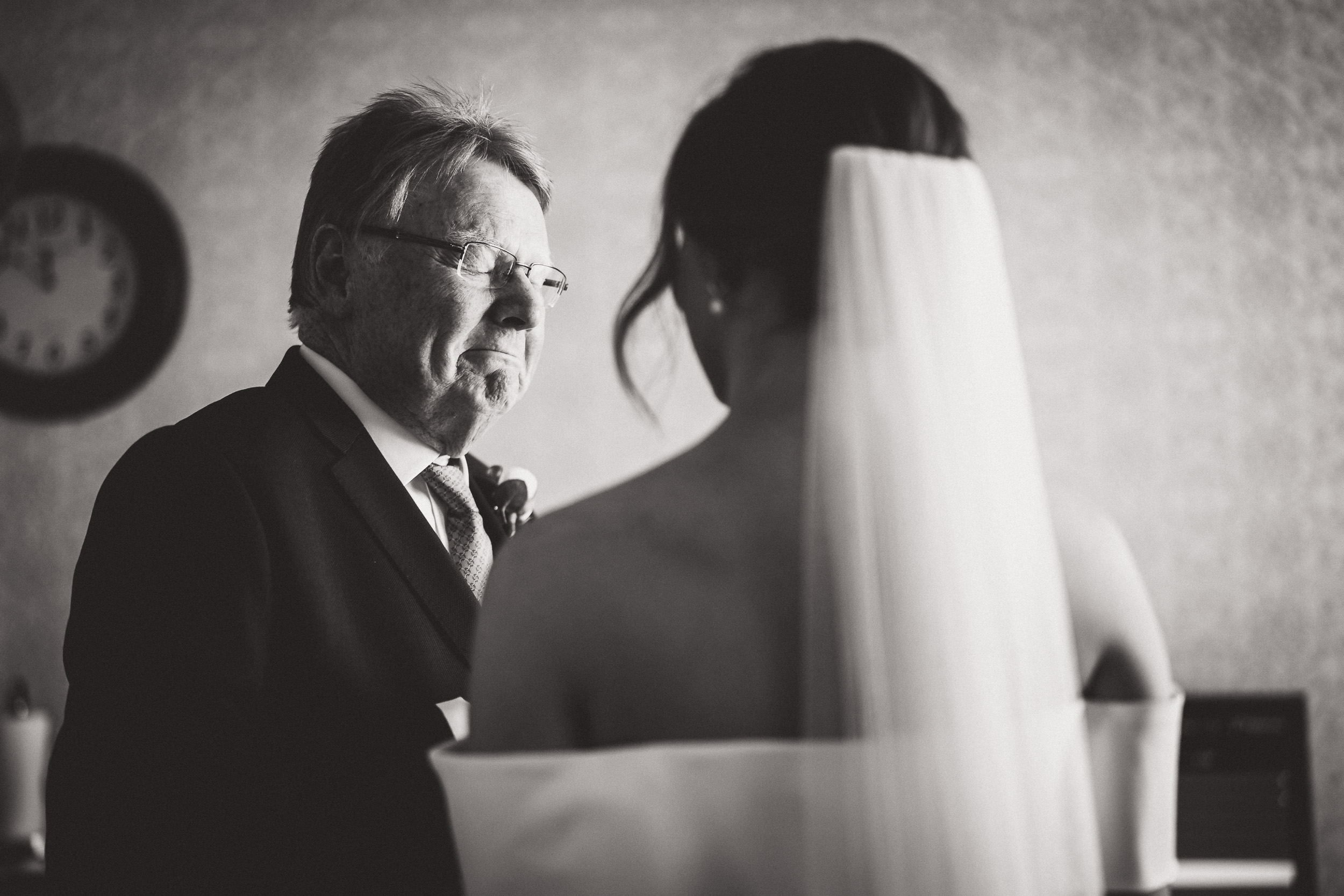 A black and white photo capturing a heartfelt moment between a bride and her father during a wedding ceremony.