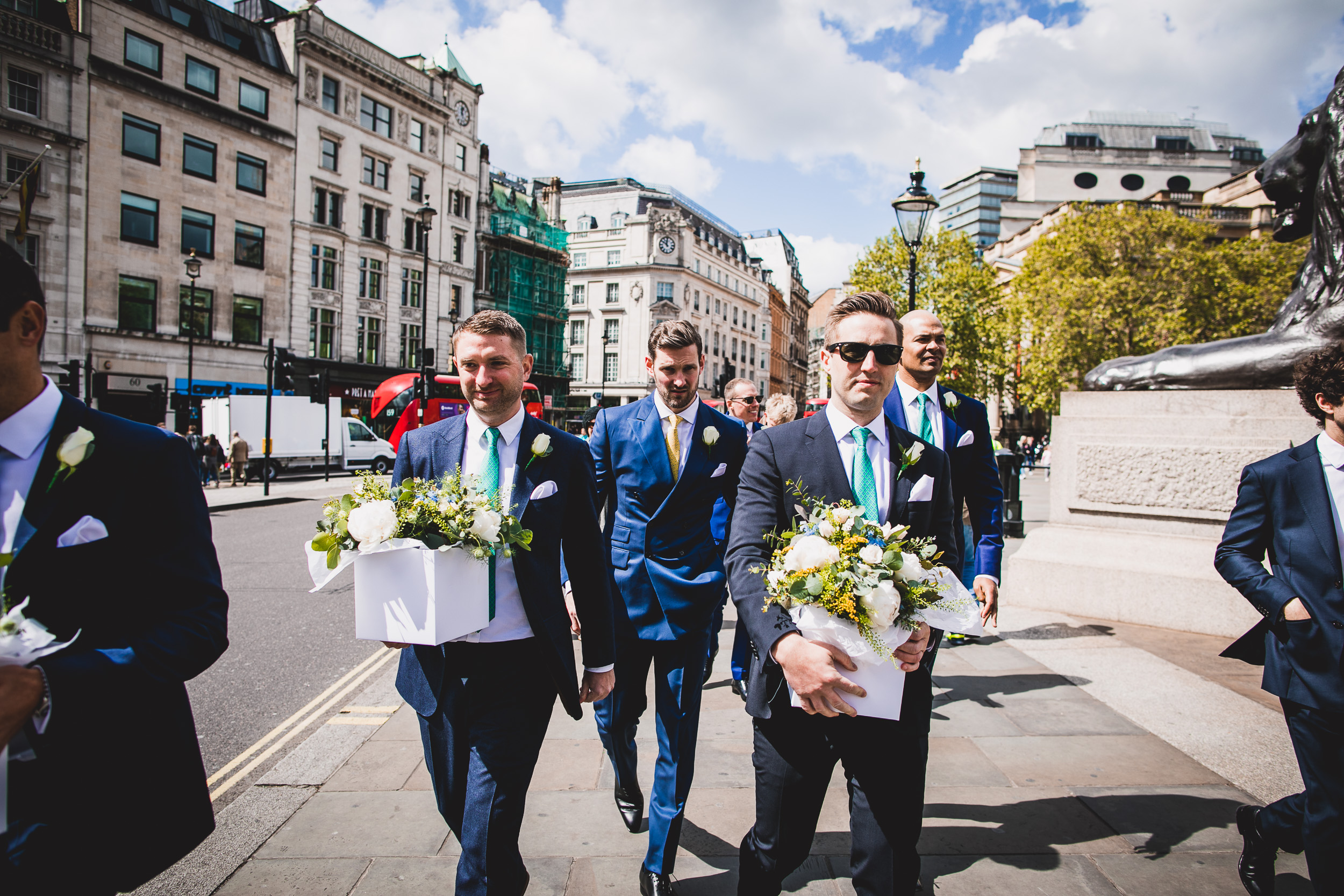 A groom and his groomsmen walking down the street to meet the bride with flowers.