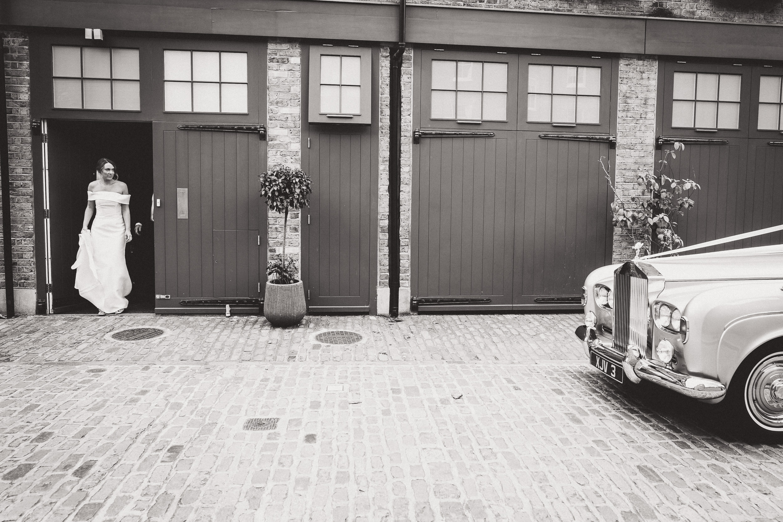 A wedding bride is standing in front of a rolls royce car.