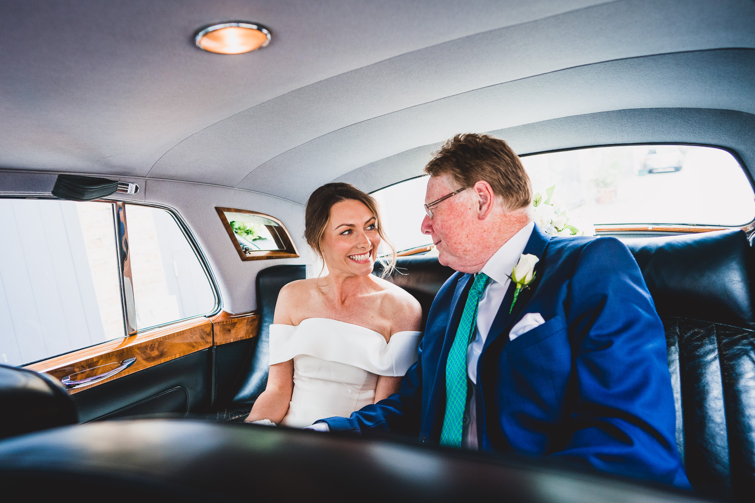 A wedding photographer captures the bride and groom seated in the back seat of a car.