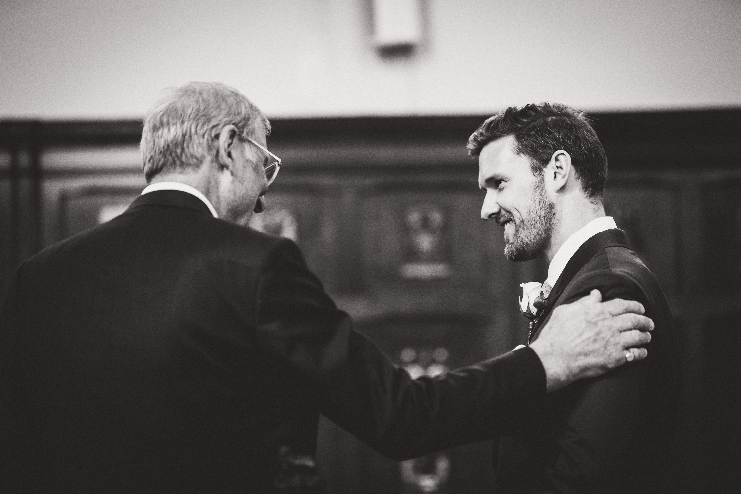 A black and white wedding photo of two grooms sharing an affectionate embrace.