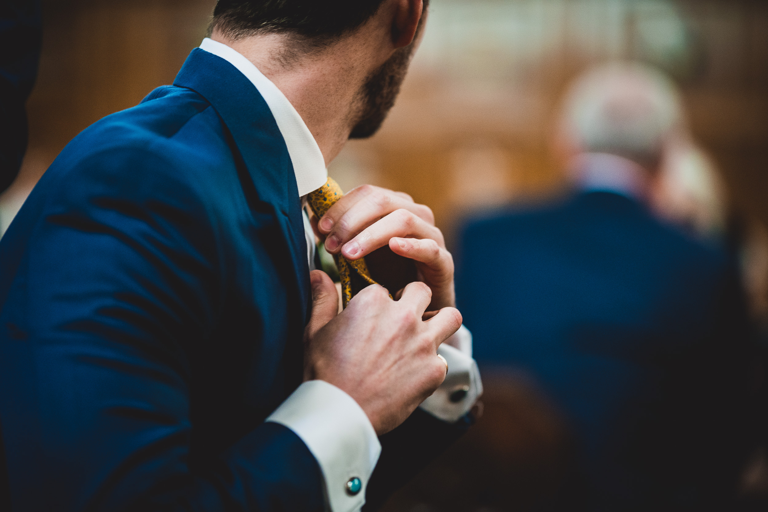 A groom in a blue suit adjusting his tie.