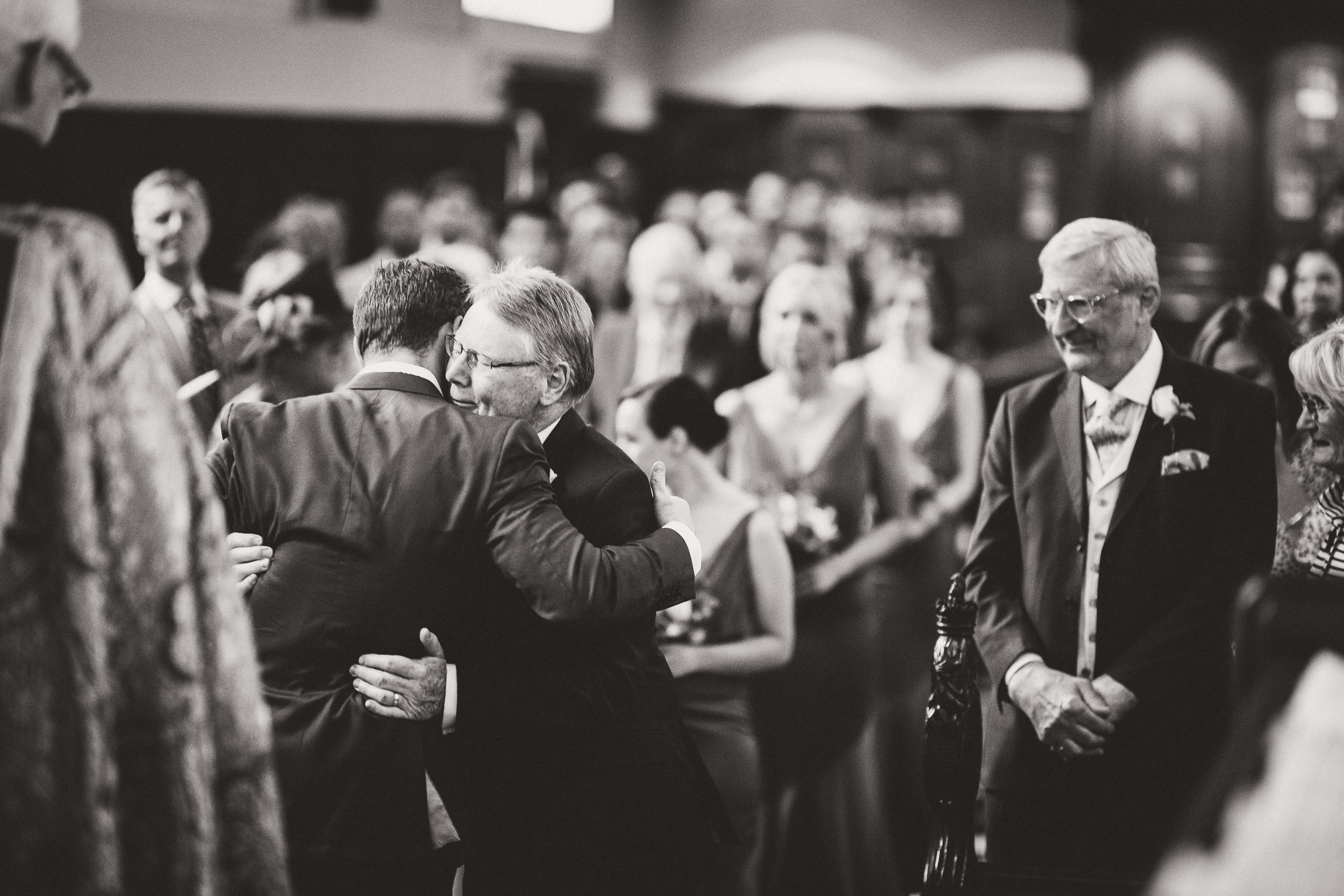 During a wedding ceremony, the groom embraces his father.