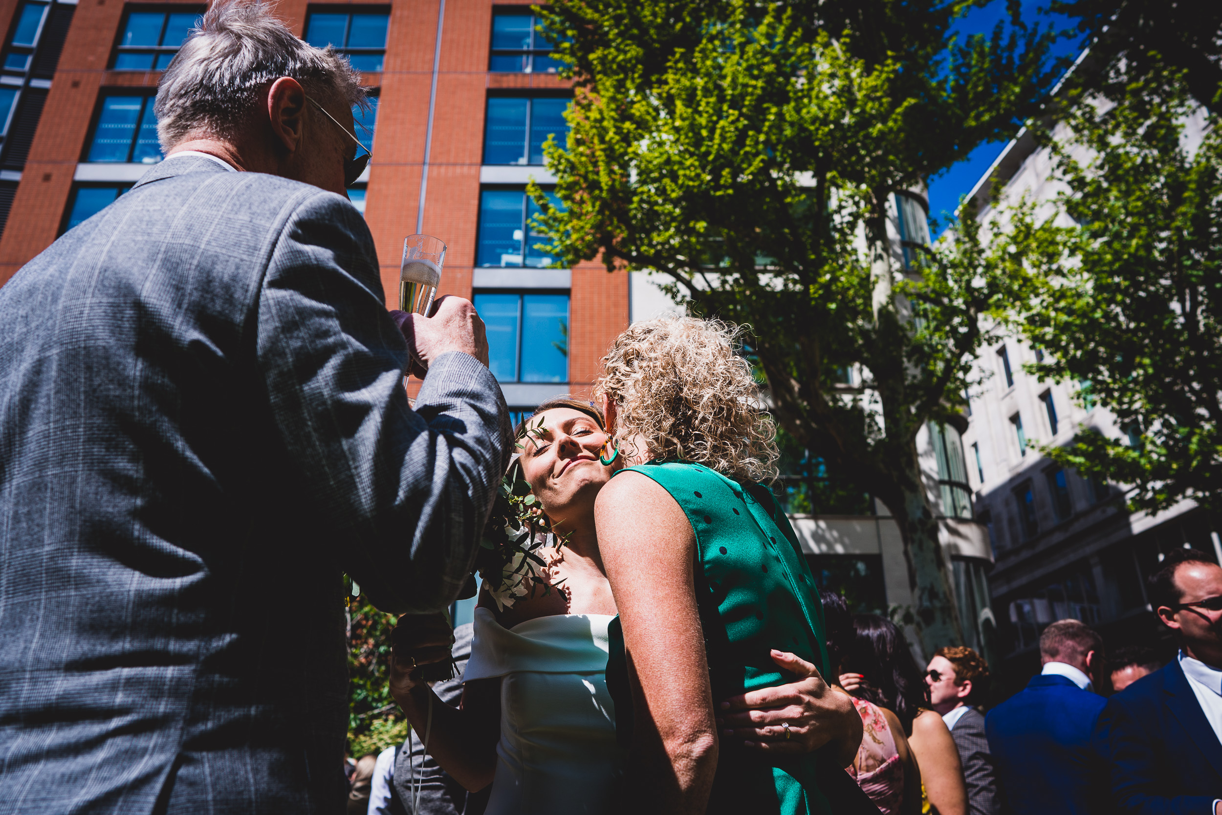 A bride holds a glass of wine in the presence of a wedding photographer capturing the moment.