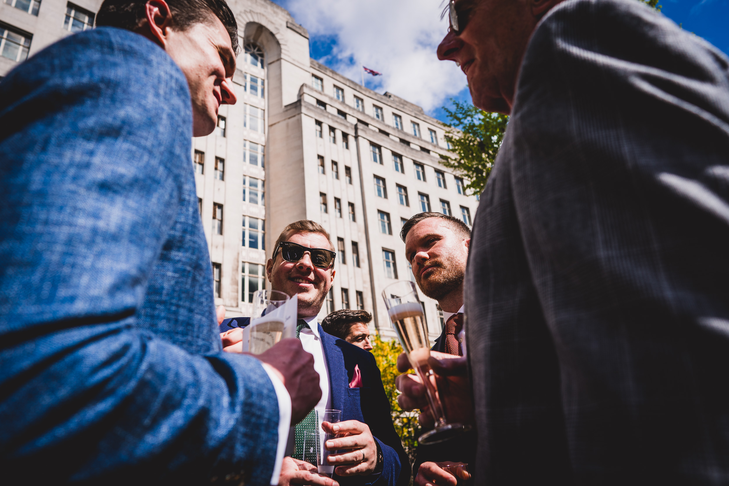 A group of men, including the groom, in suits talking outside of a building.