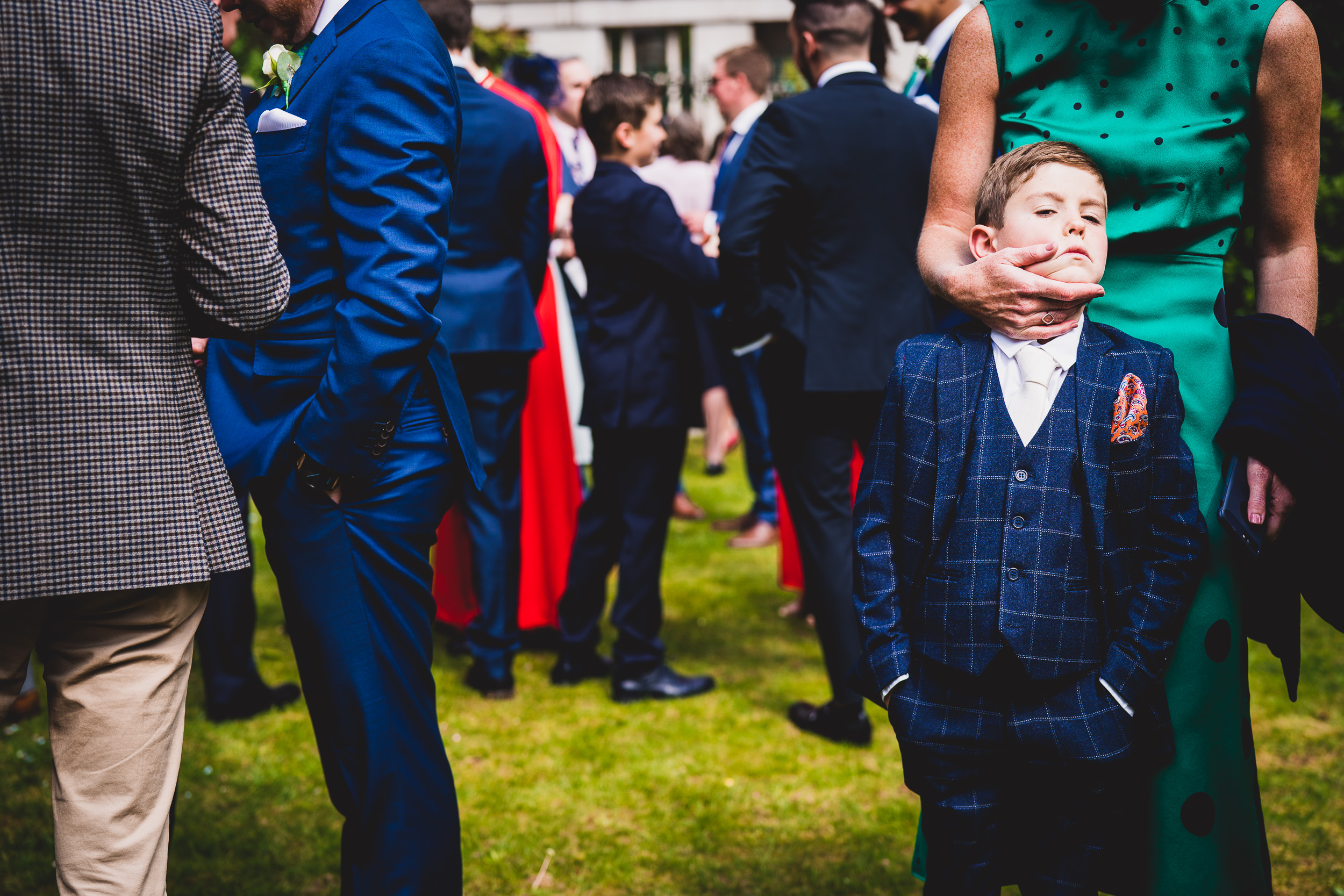 A little groom in a suit standing next to a wedding party for his wedding photo.