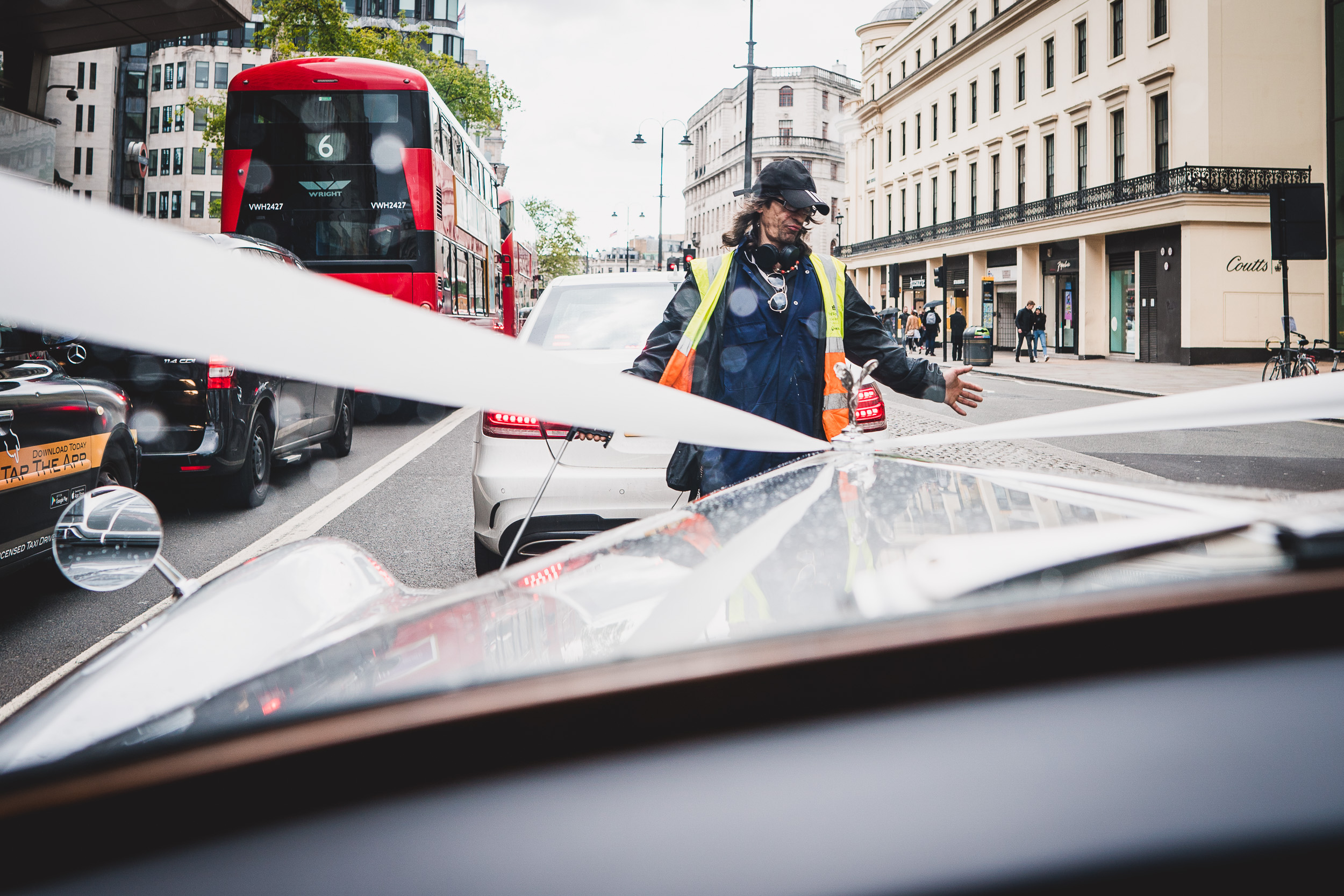 A wedding photographer captures the groom cutting a ribbon on the side of a car.