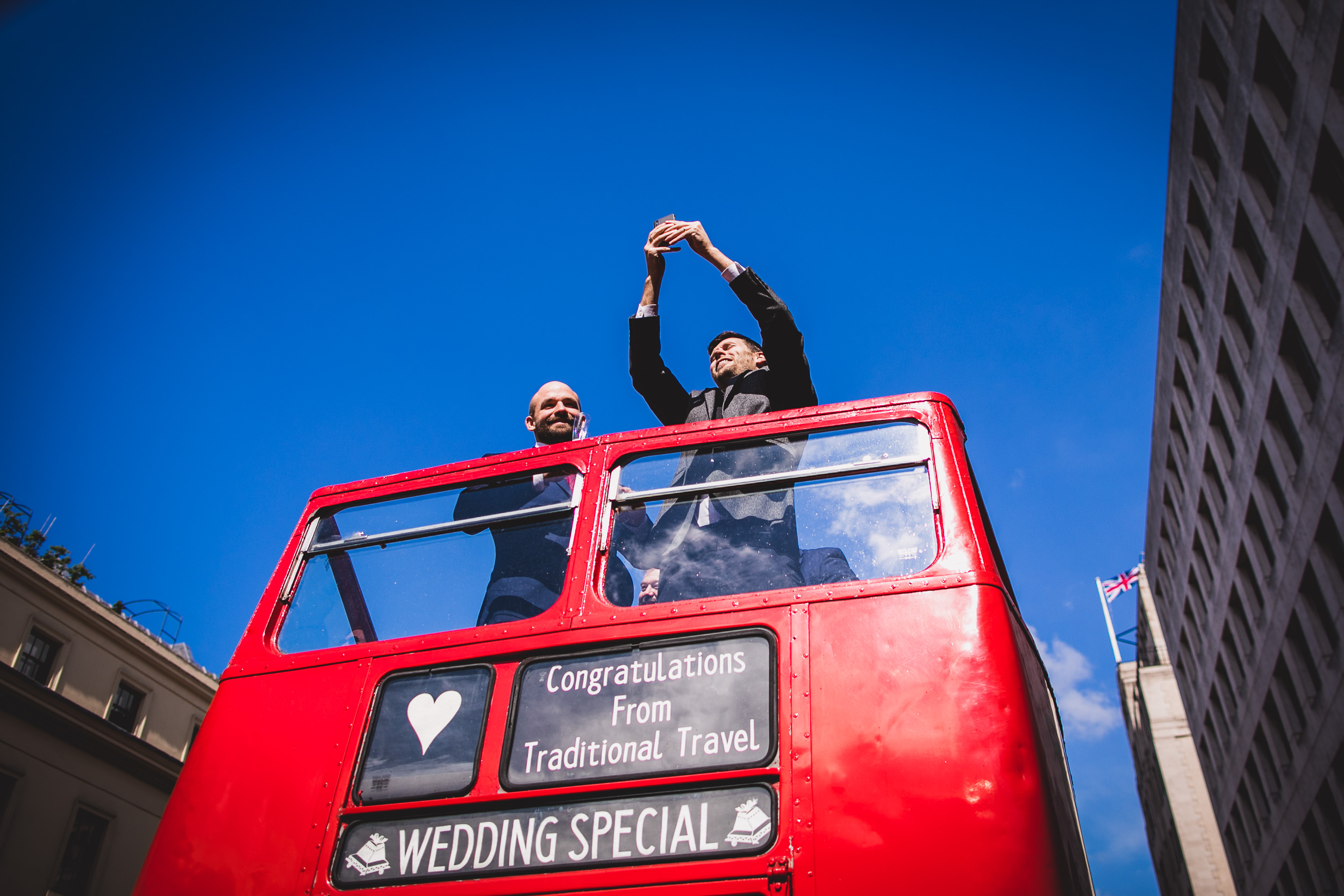 Two grooms pose for a wedding photo on a double decker bus.