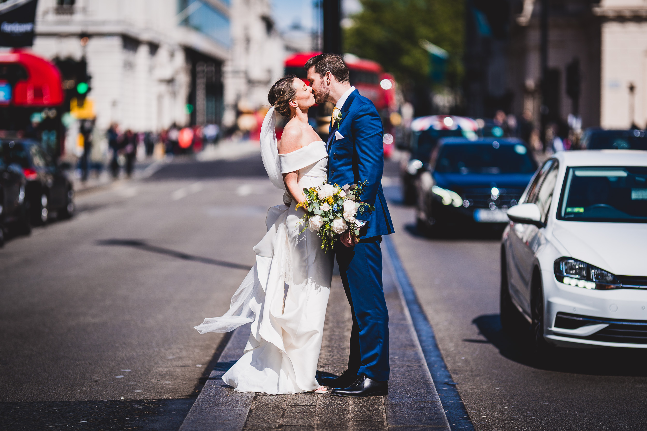 A wedding photographer captures a kiss between a bride and groom on the streets of London.