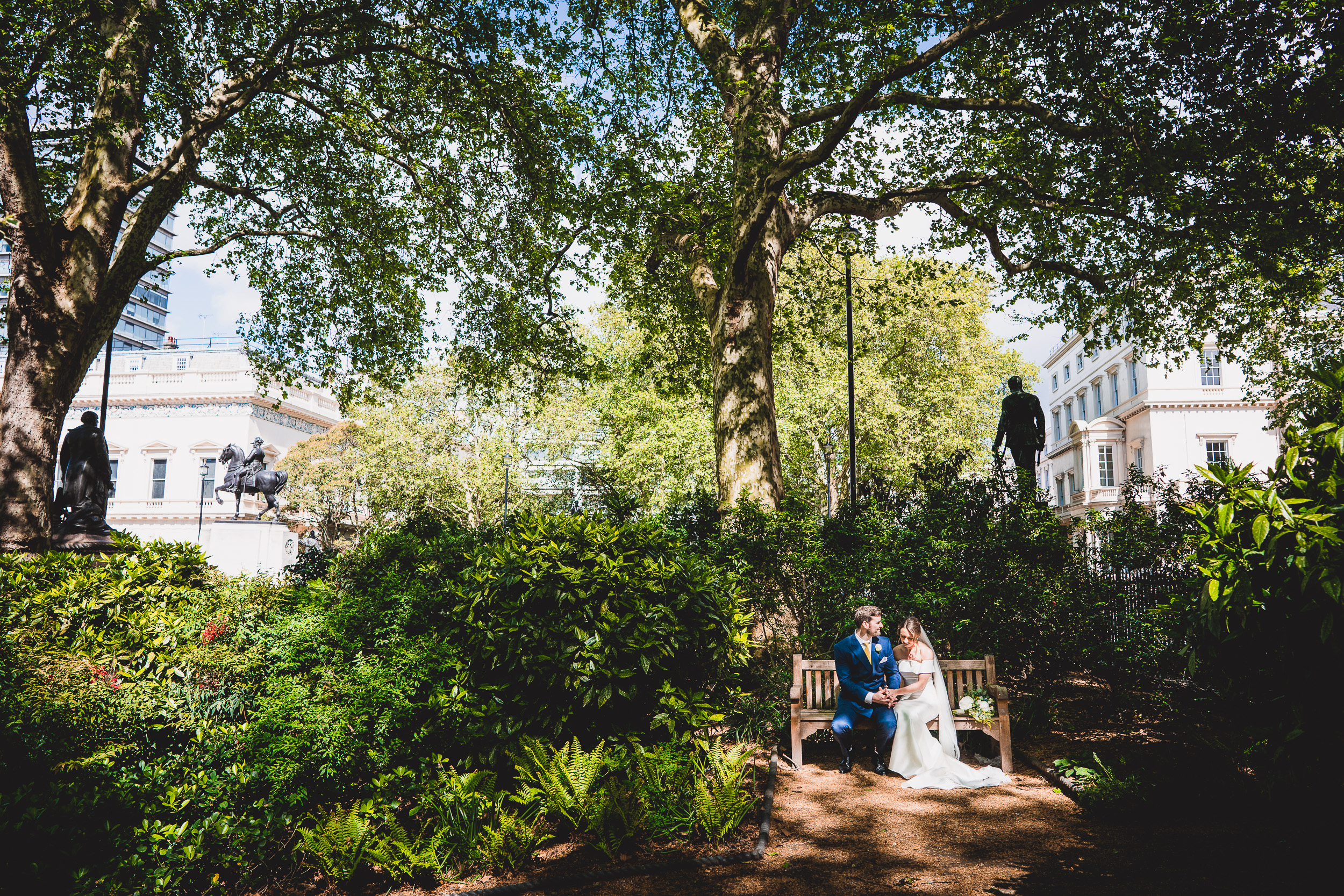 A bride and groom captured in a wedding photo while sitting on a garden bench.