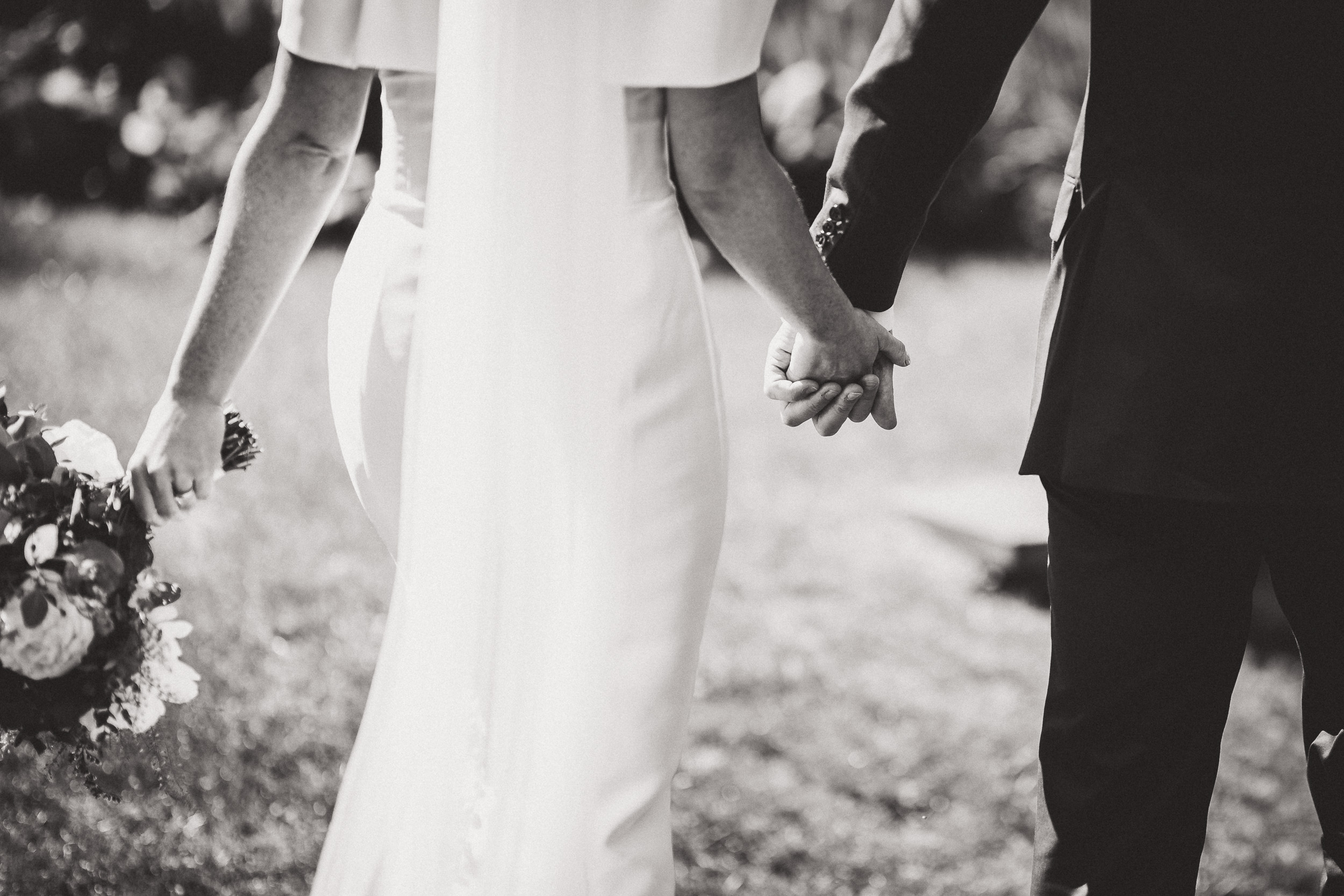 A black and white photo capturing the special moment of a bride and groom holding hands, taken by a wedding photographer.