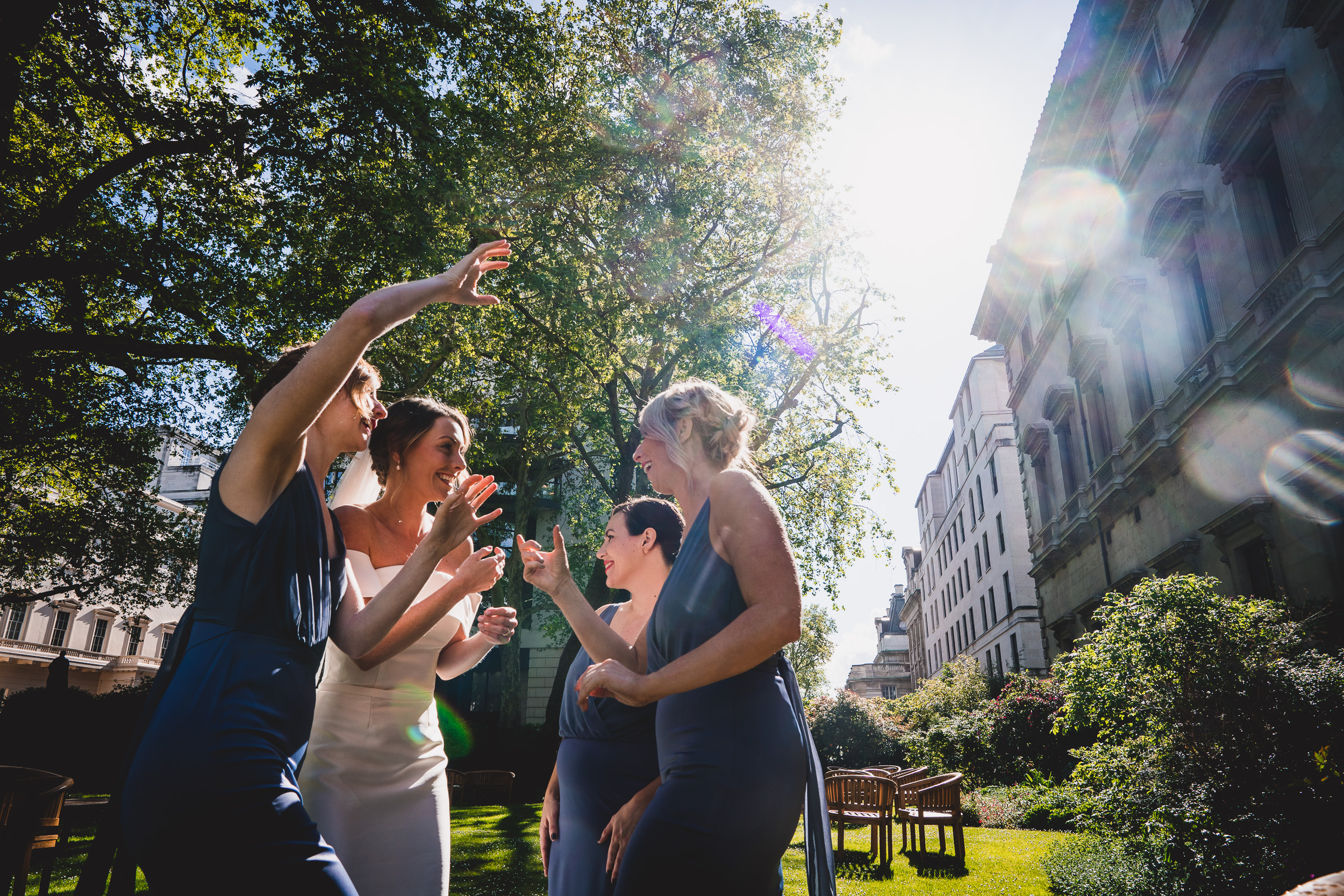 A wedding party including bridesmaids celebrating in the sun with the bride and a wedding photographer.