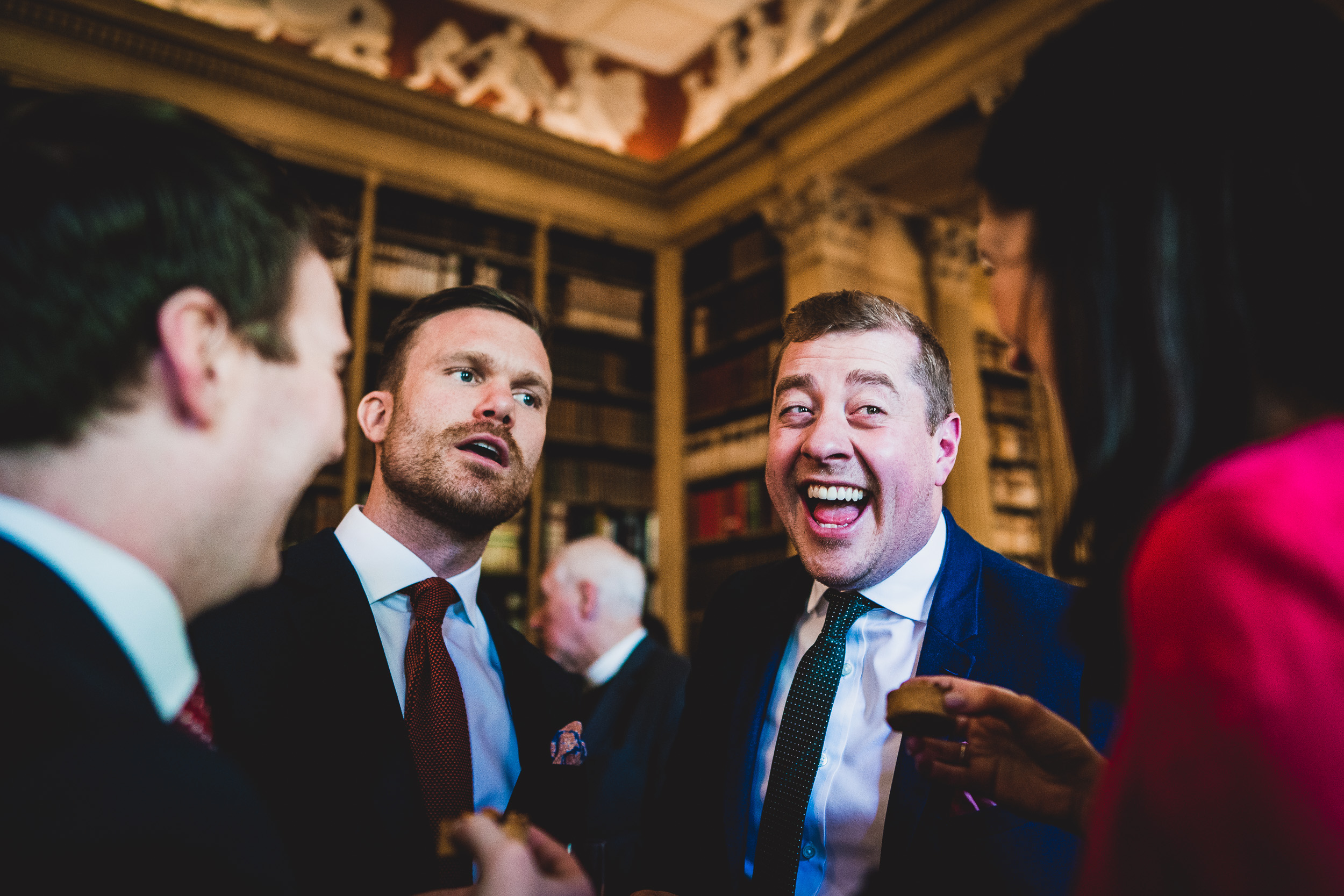 A wedding photographer captures the bride and group laughing in a library.