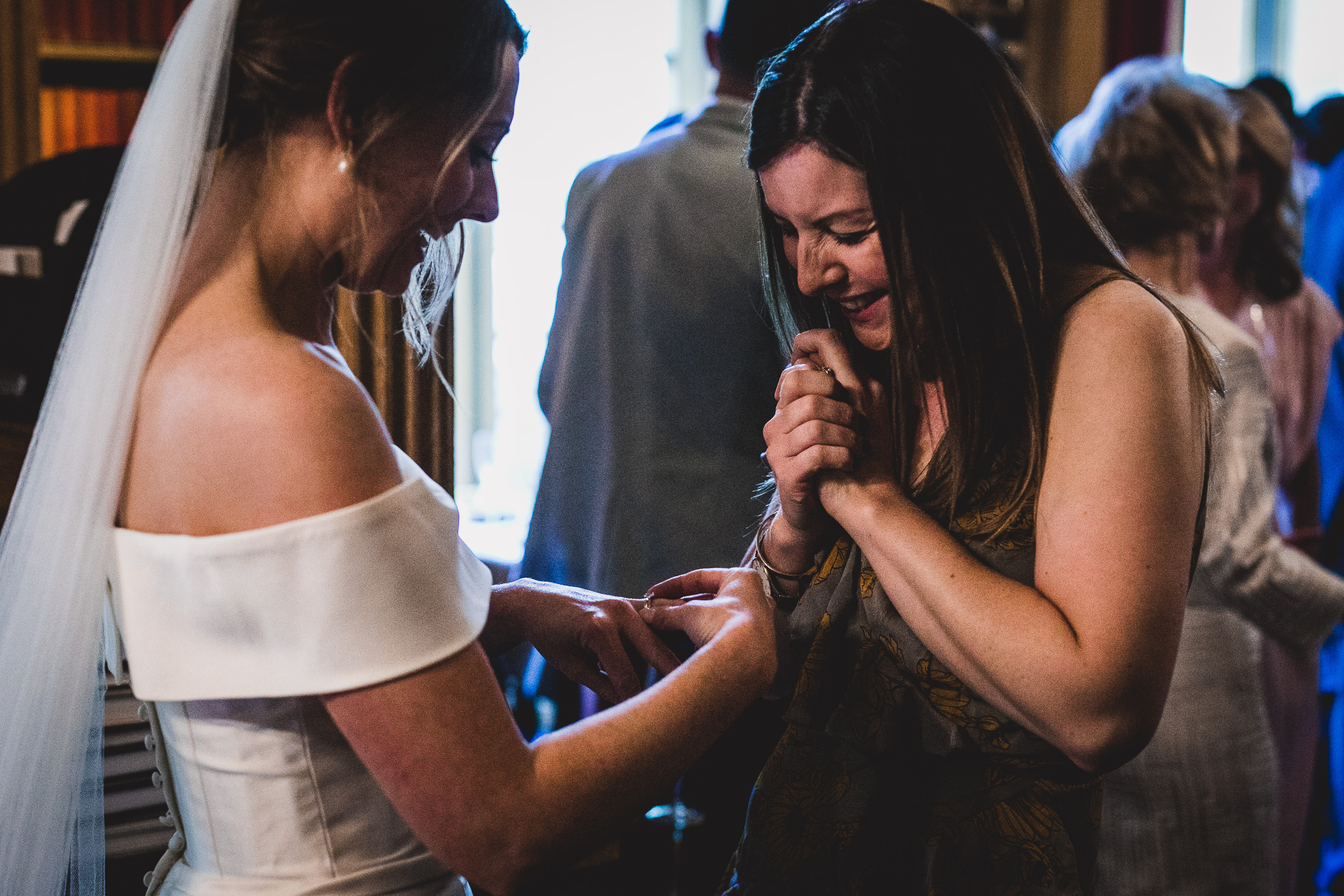 A wedding photographer captures the moment a woman helps another woman put on her wedding ring, alongside the groom.