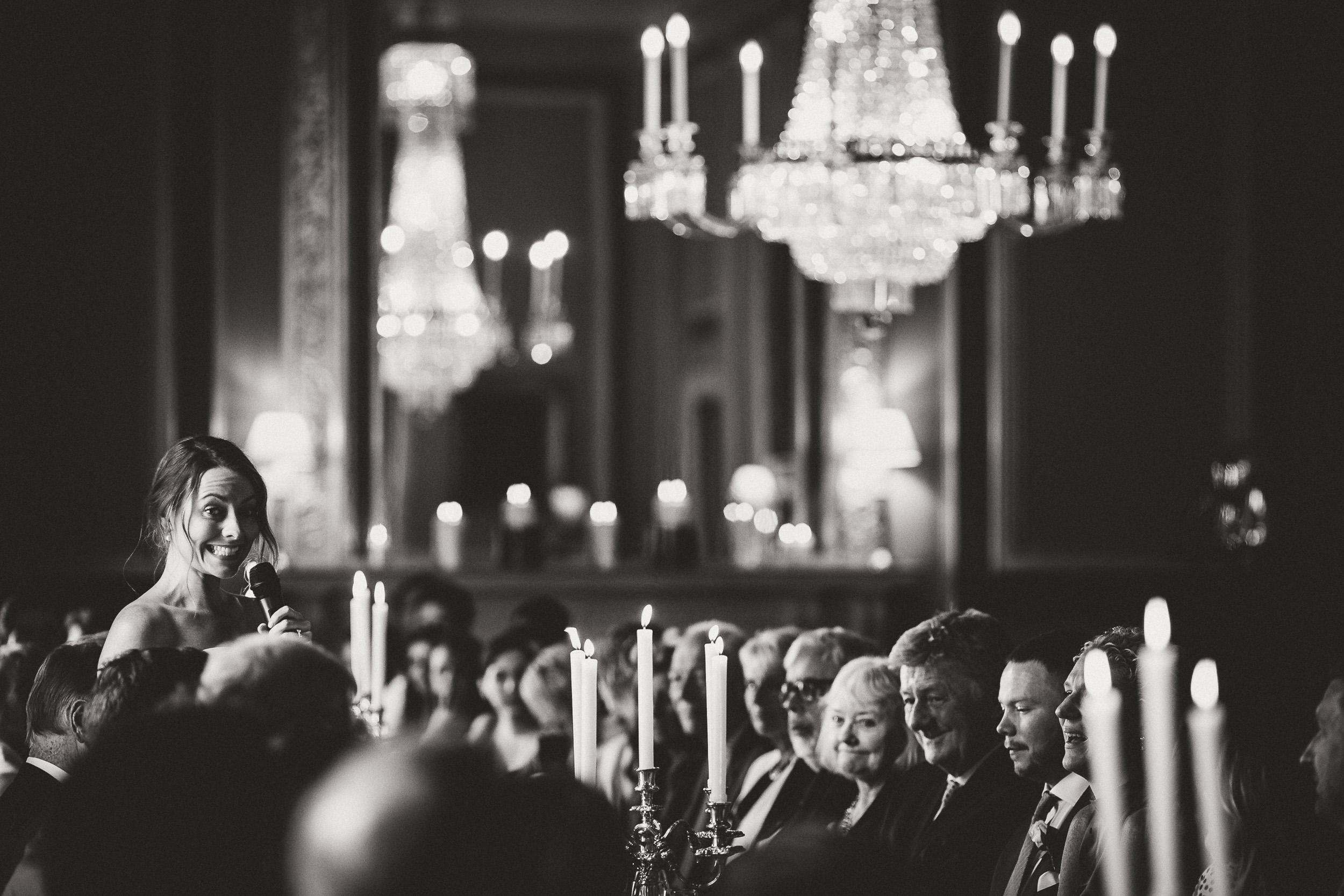 A black and white photo of a wedding with the woman speaking at the groom's side.