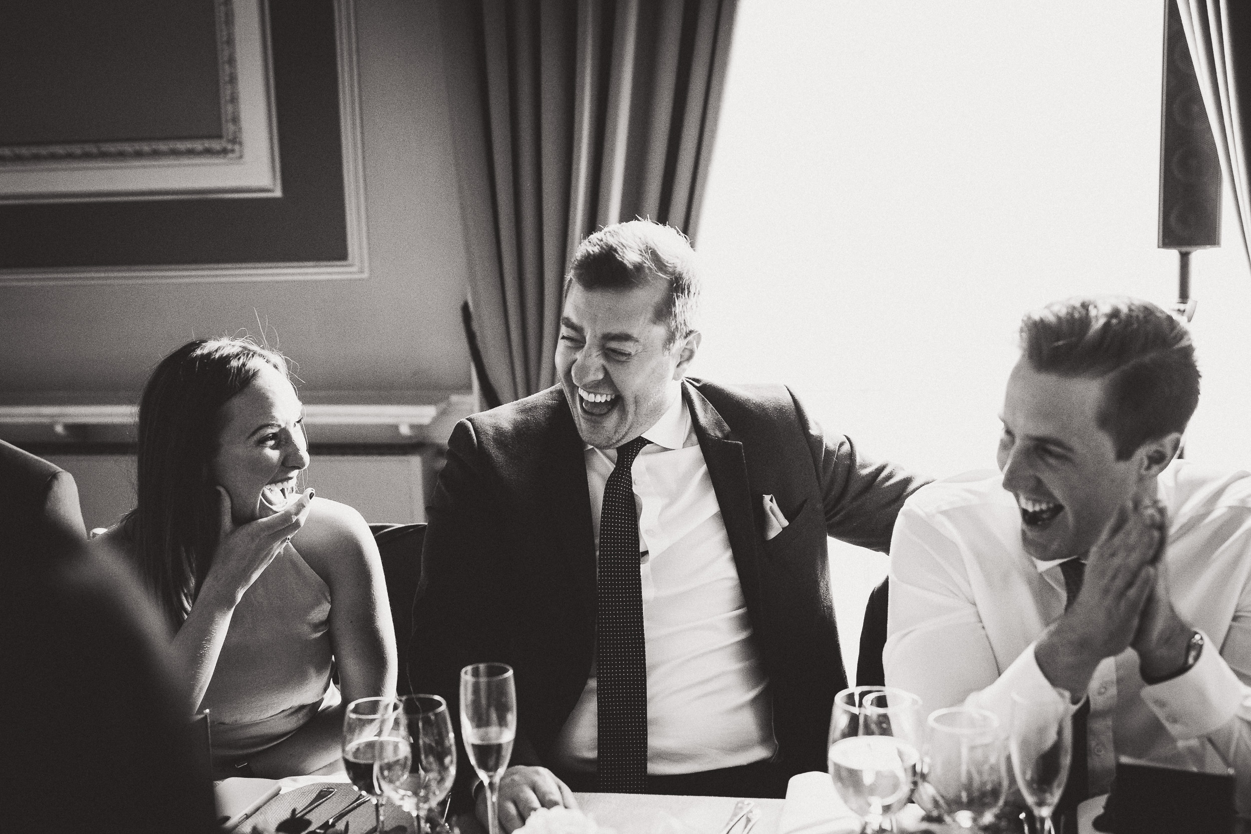 A wedding photographer captured a black and white groom's photo featuring a group of people laughing at a table.