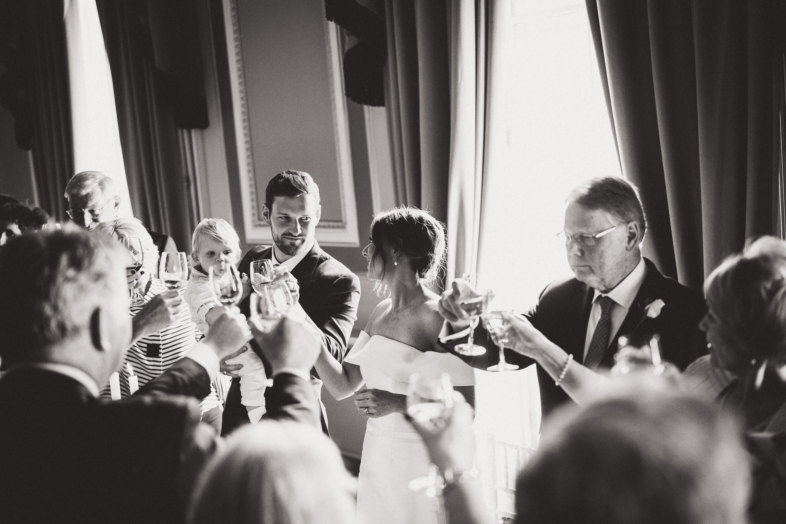 A wedding photographer captures a black and white photo of the bride and groom toasting.